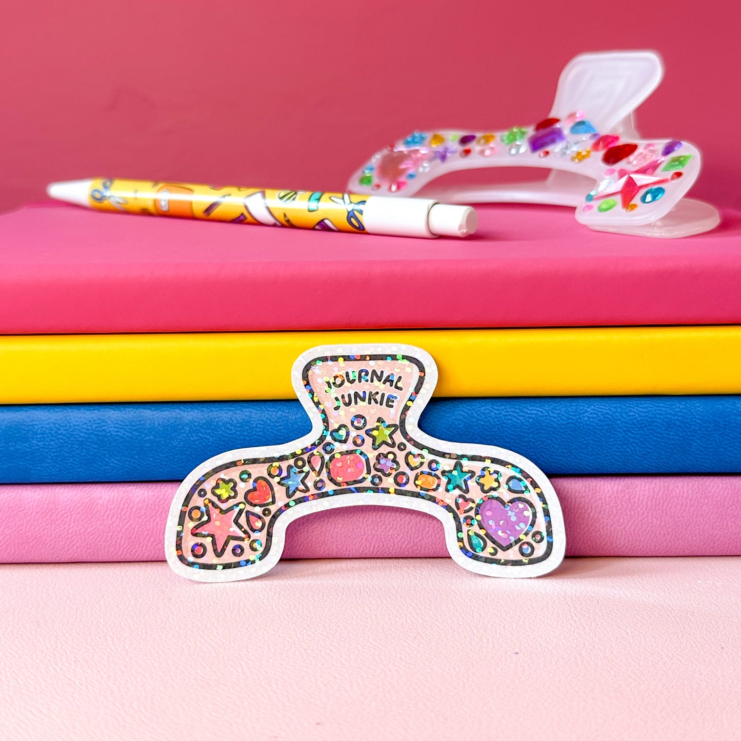 Colorful stationery items including a pen, colorful heart-patterned object, and 'Journal Junkie' sticker on pink and blue notebooks.