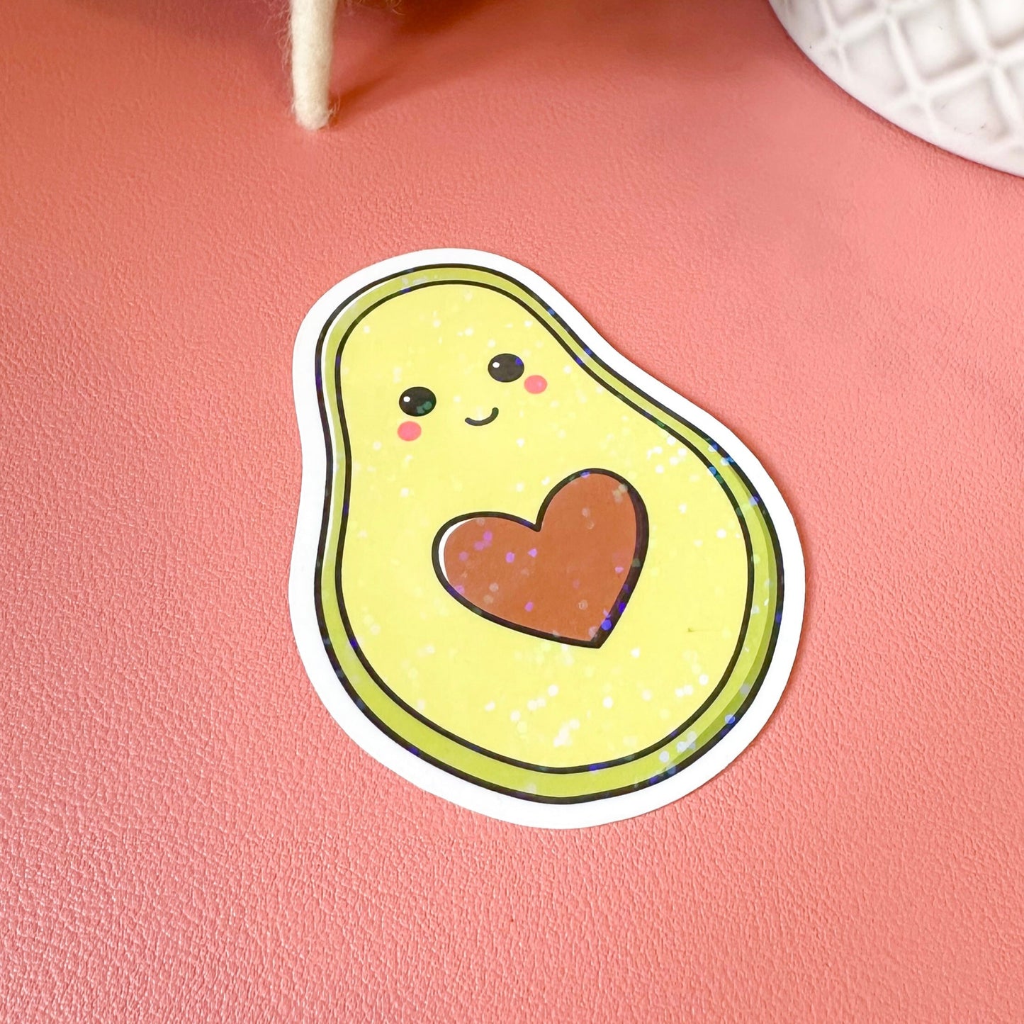 Sticker of a cartoon avocado with a heart on a pink surface