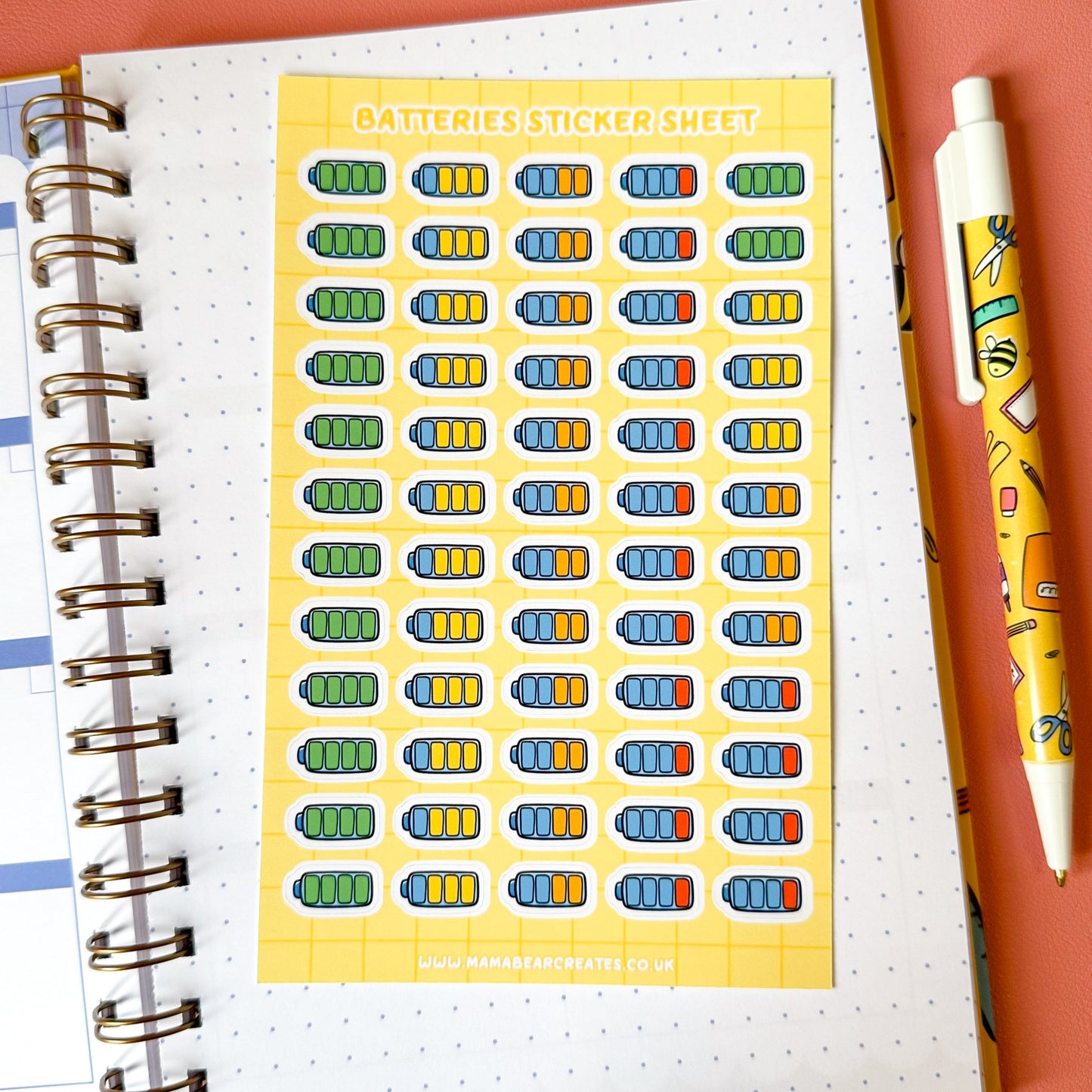 Sheet of colorful battery stickers on a notebook with a pen on a pink background