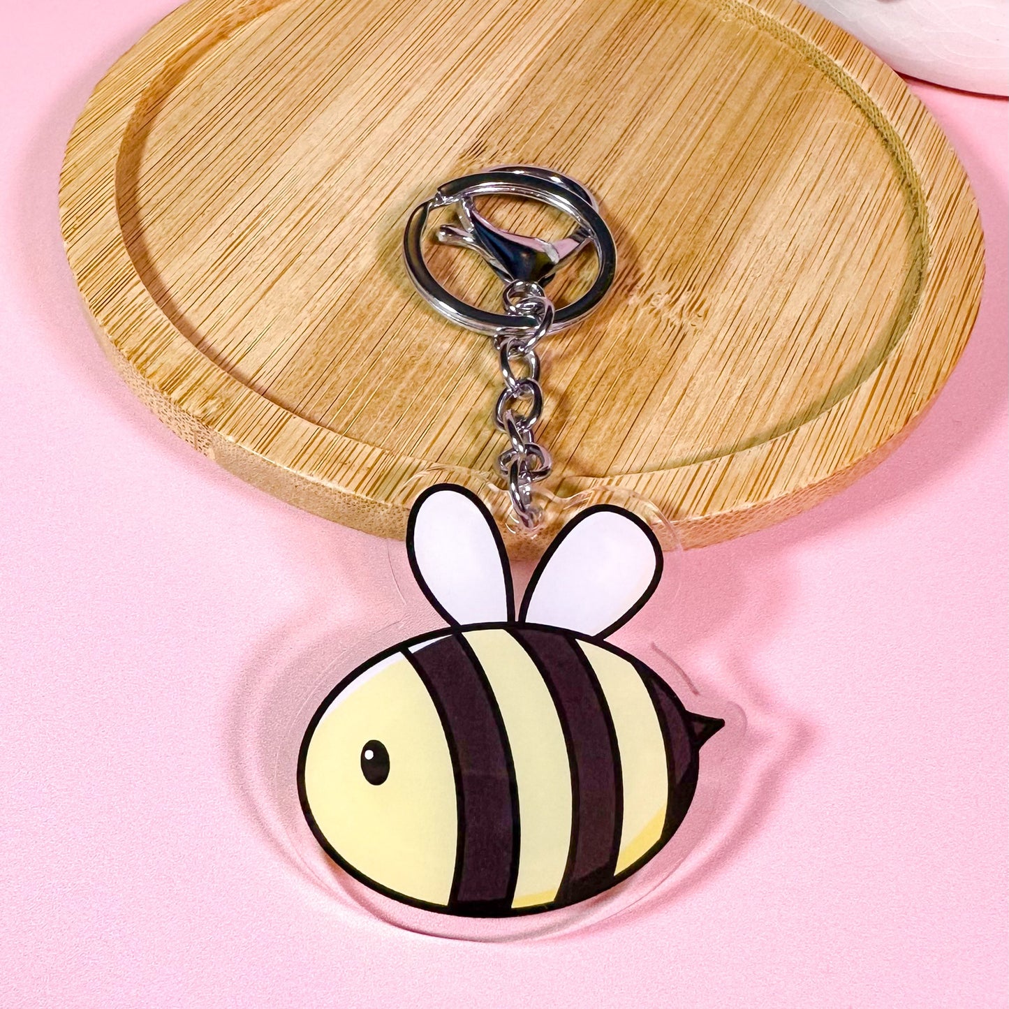 Bee-shaped keychain on a wooden tray with a pink background
