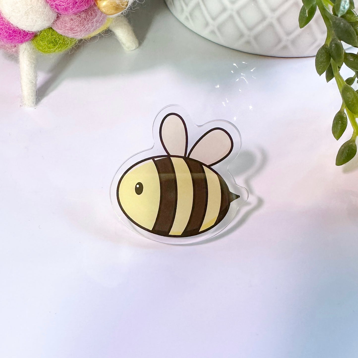 A pin badge featuring a design of a yellow and black striped bee with white wings, presented on a clear background.