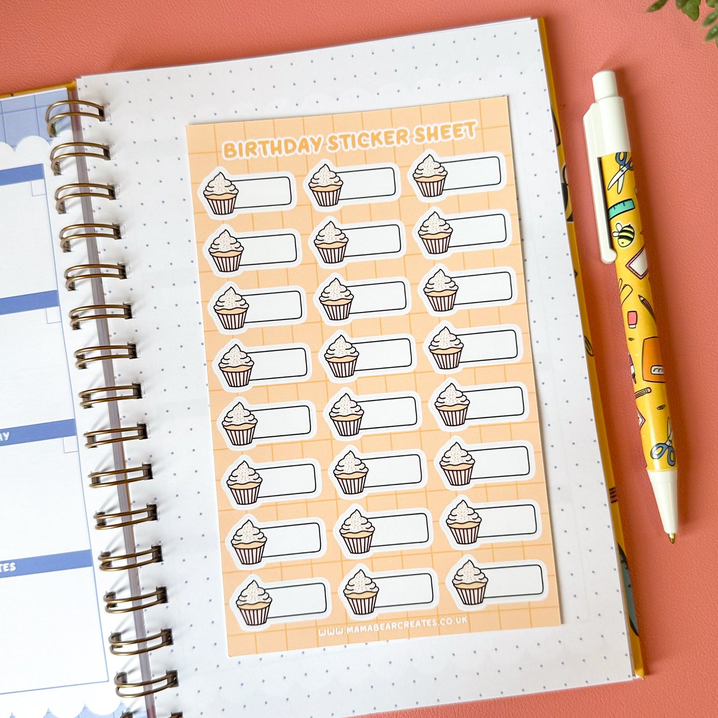Sheet of birthday stickers with a pen and planner on a pink surface