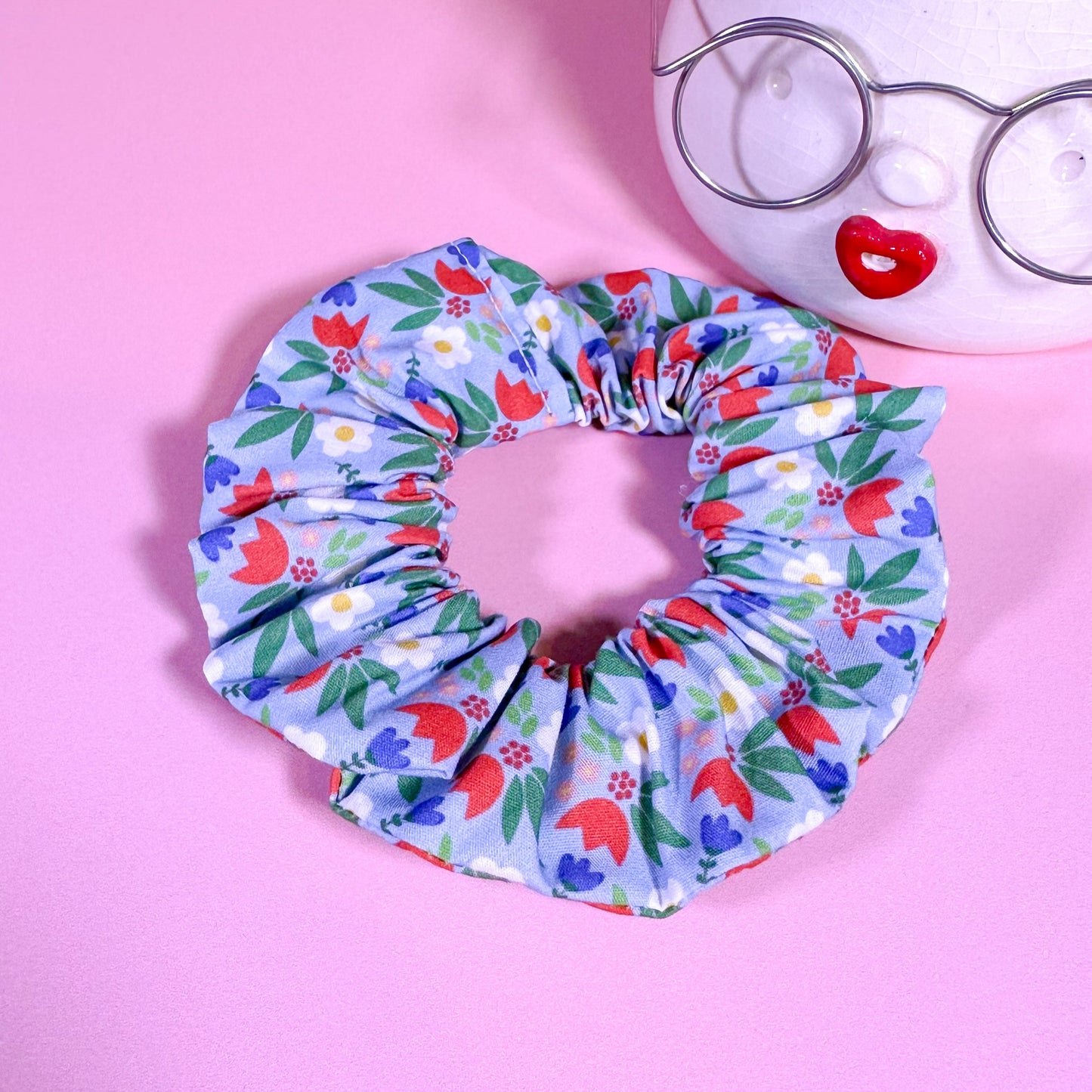 Floral patterned scrunchie on a pink background with a plant and glasses.