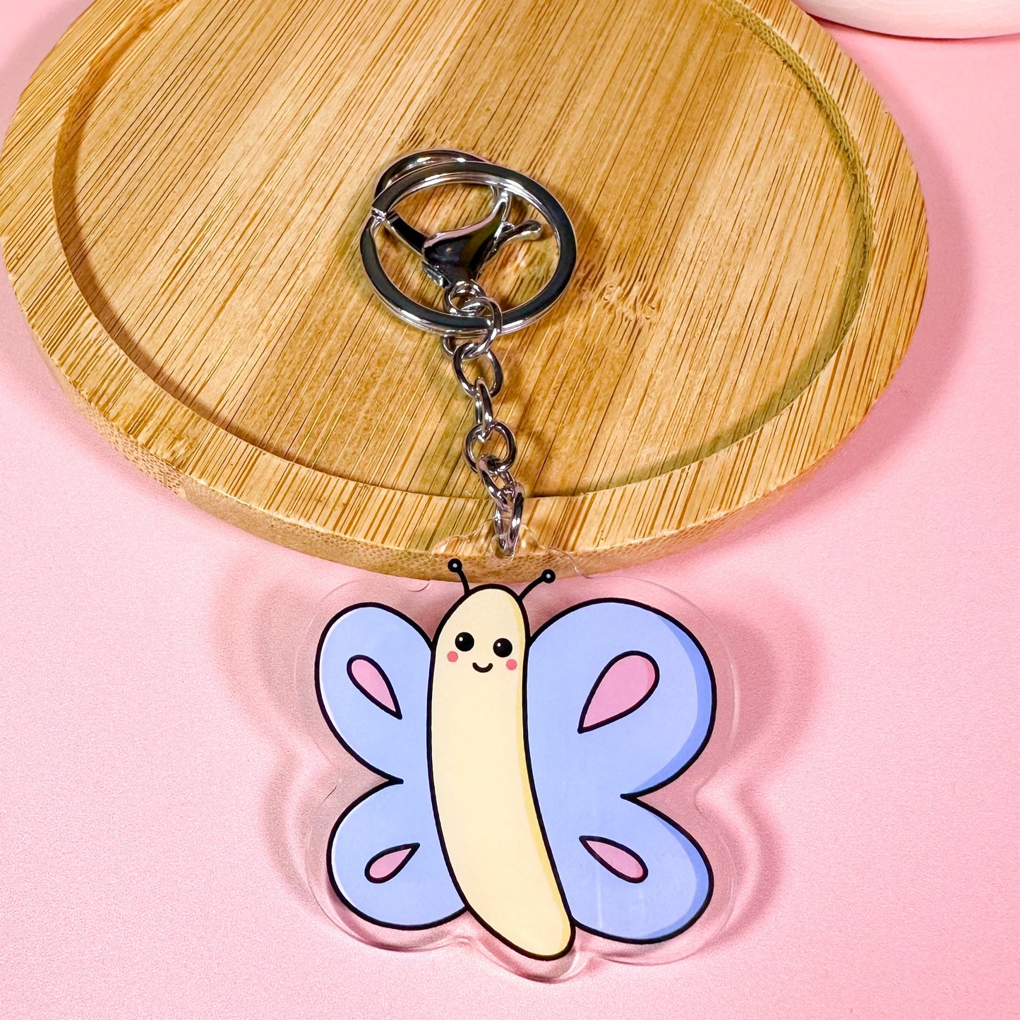 Butterfly-shaped keychain on a wooden tray with a pink background