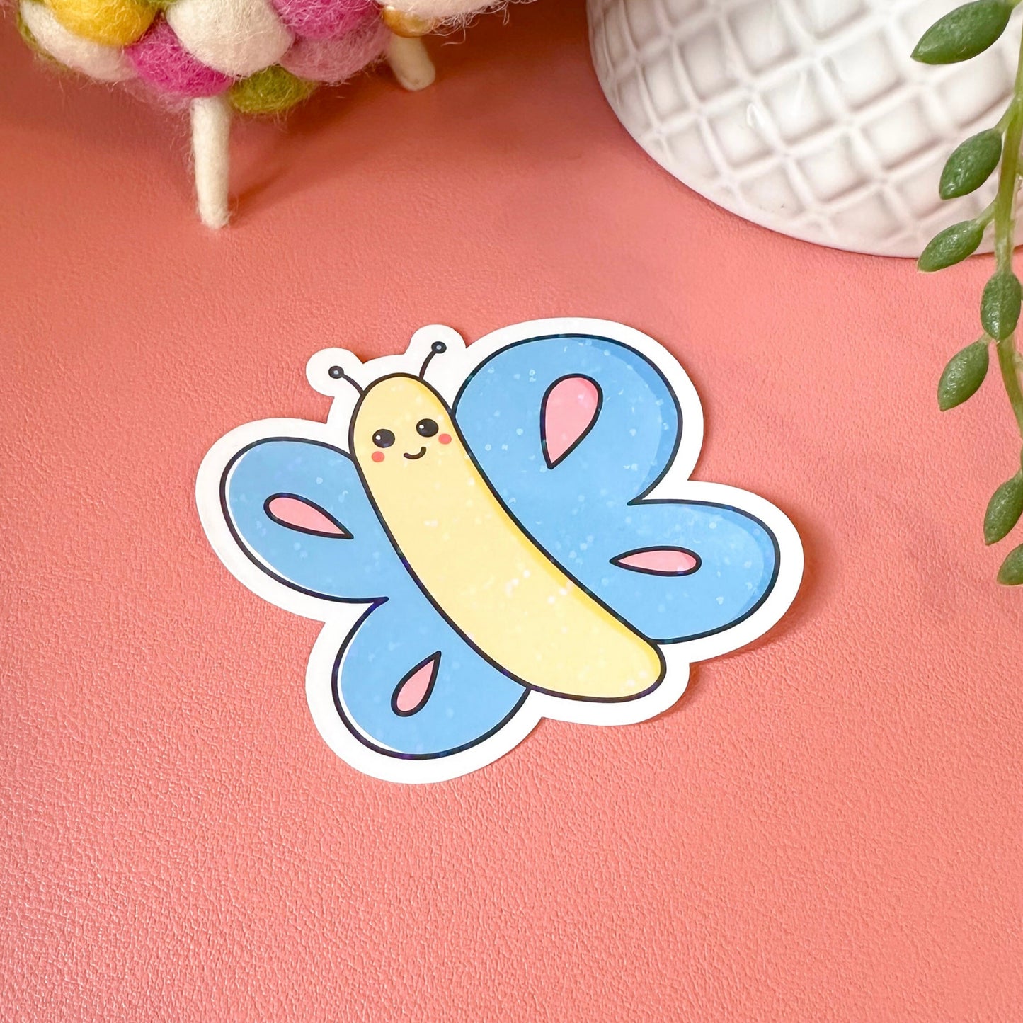 Cartoonish caterpillar with butterfly wings sticker on a pink surface