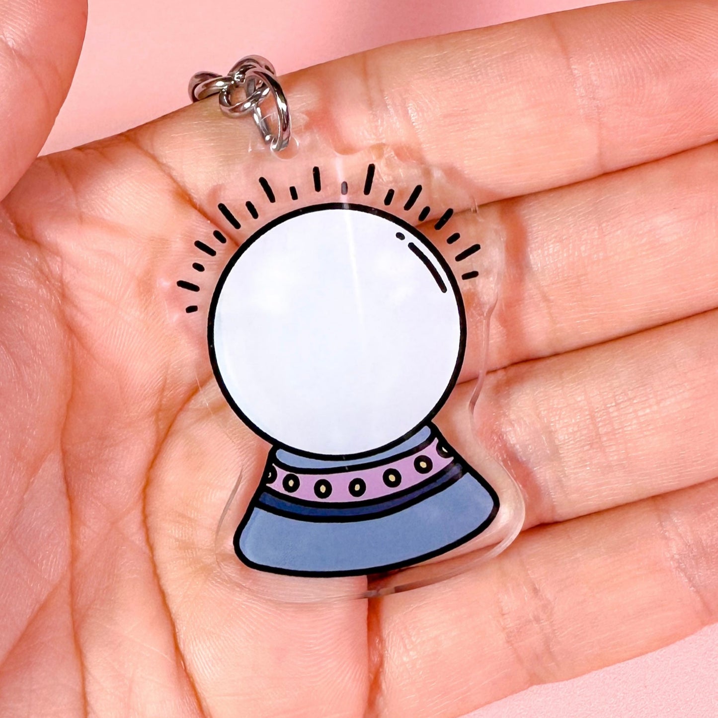 Keychain with a crystal ball design held in a hand against a pink background