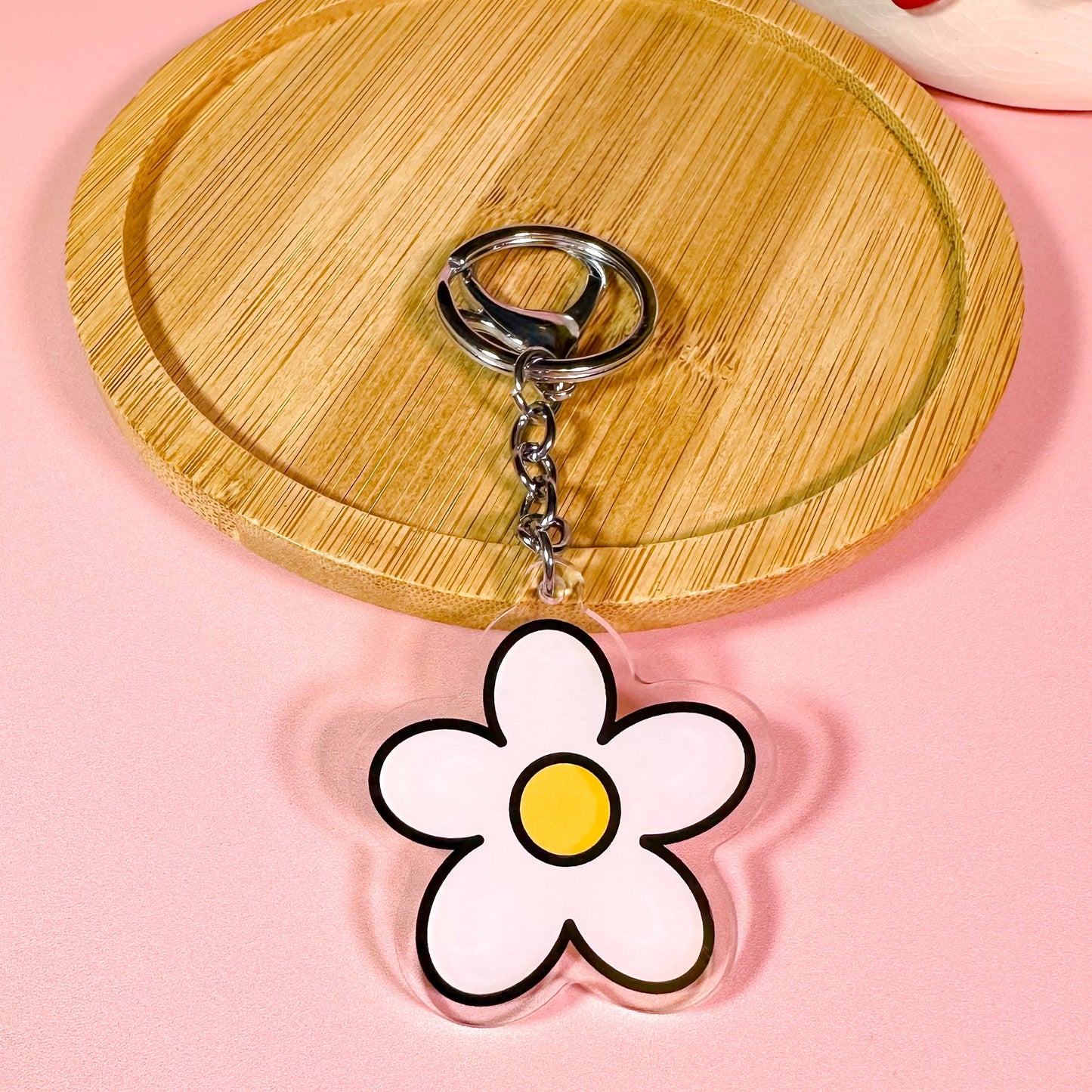 Flower-shaped keychain on a pink background with a wooden coaster
