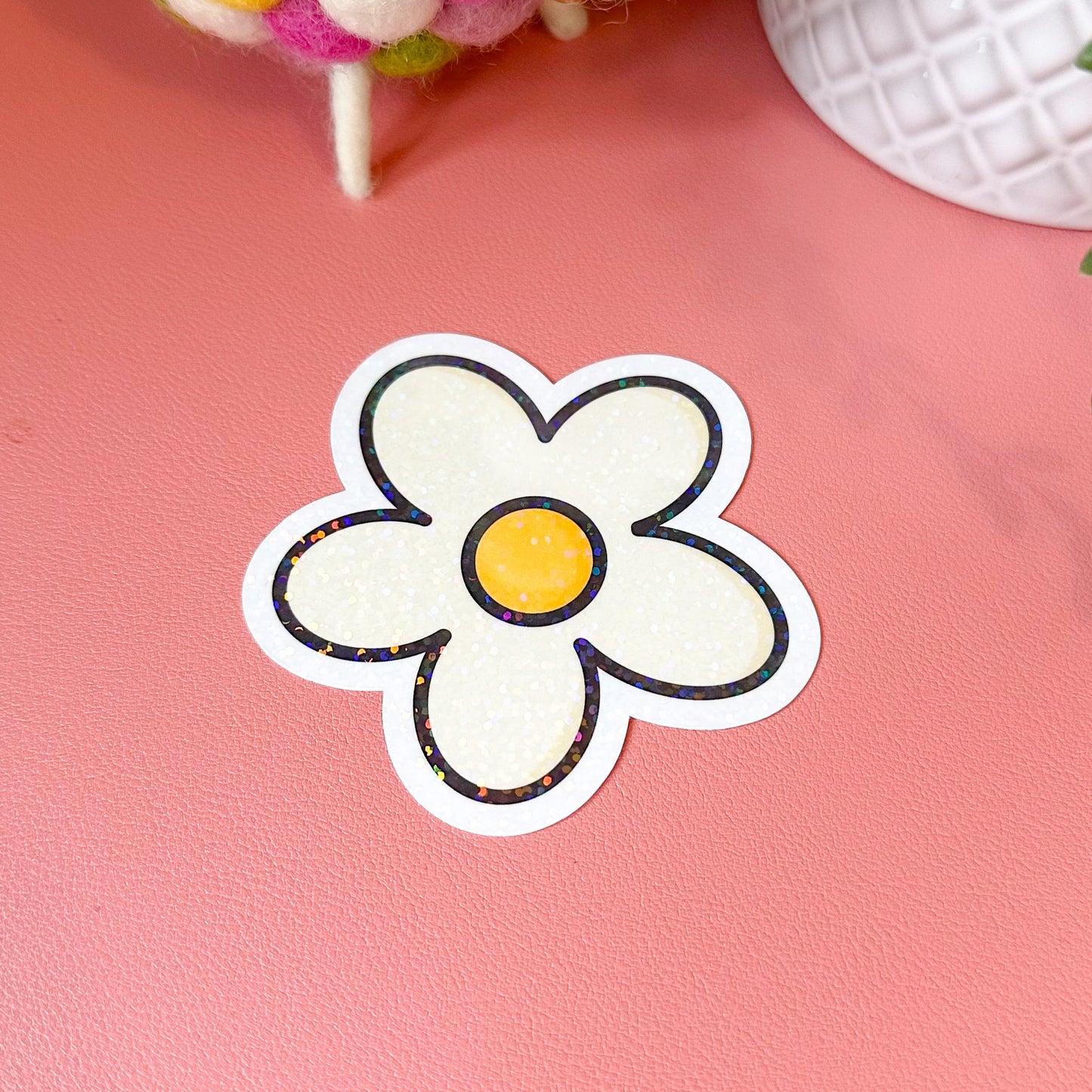 Flower-shaped sticker on a pink surface with a toy and plant in the background