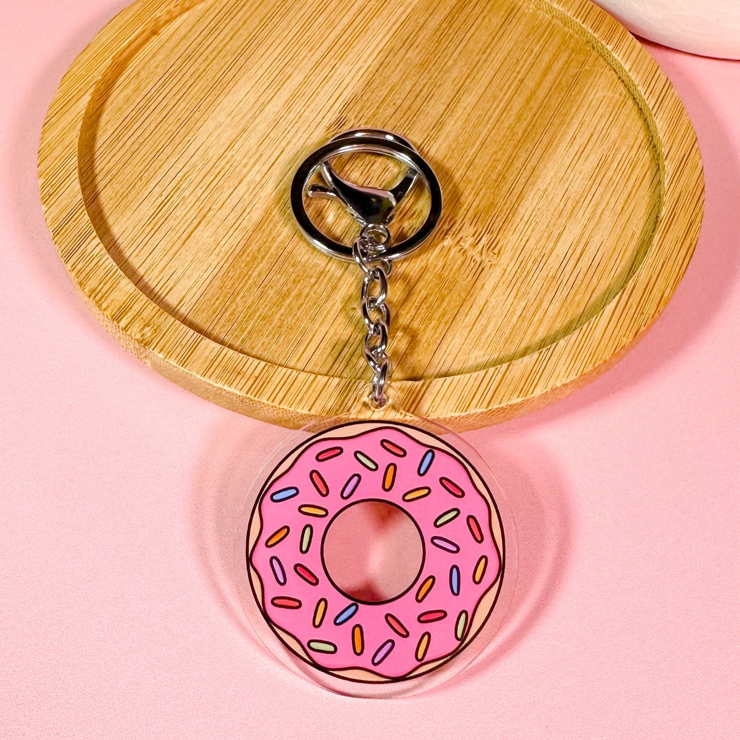 Pink donut keychain on a wooden coaster with a pink background