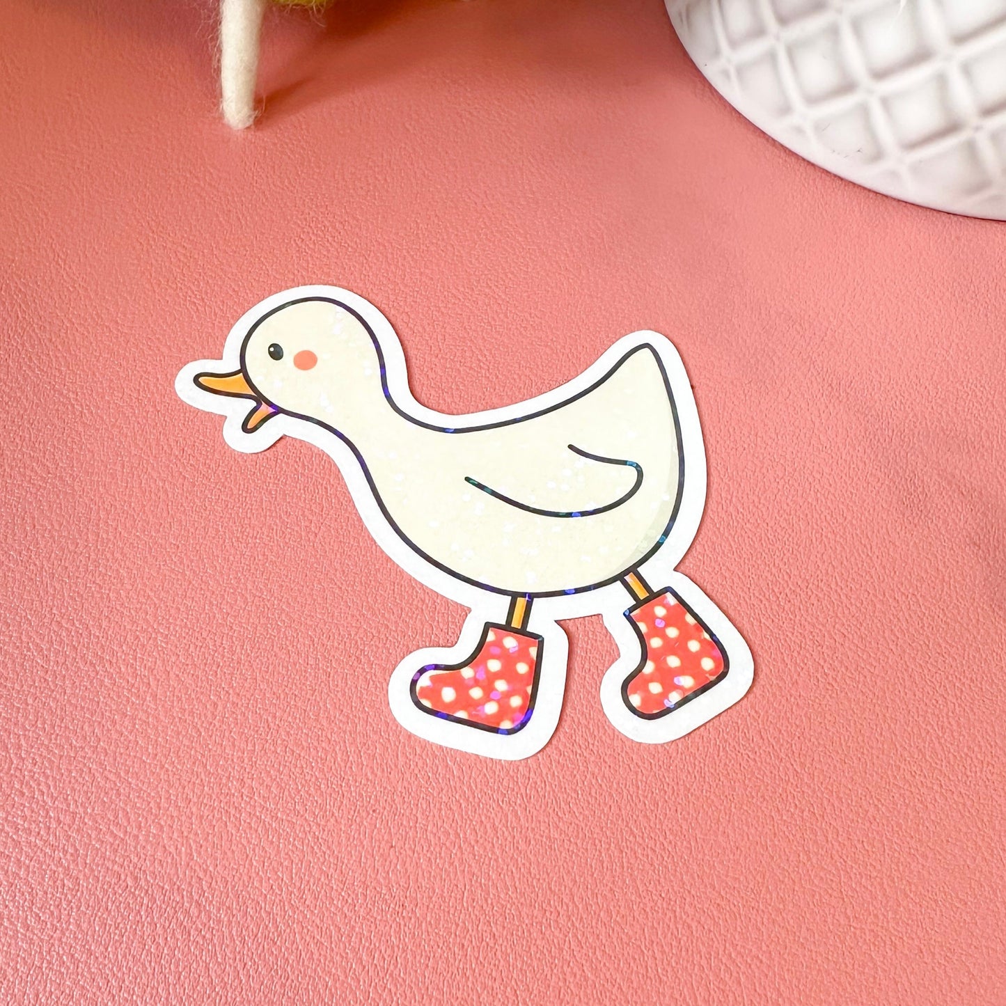 Cartoon duck sticker with polka dot shoes on a pink surface