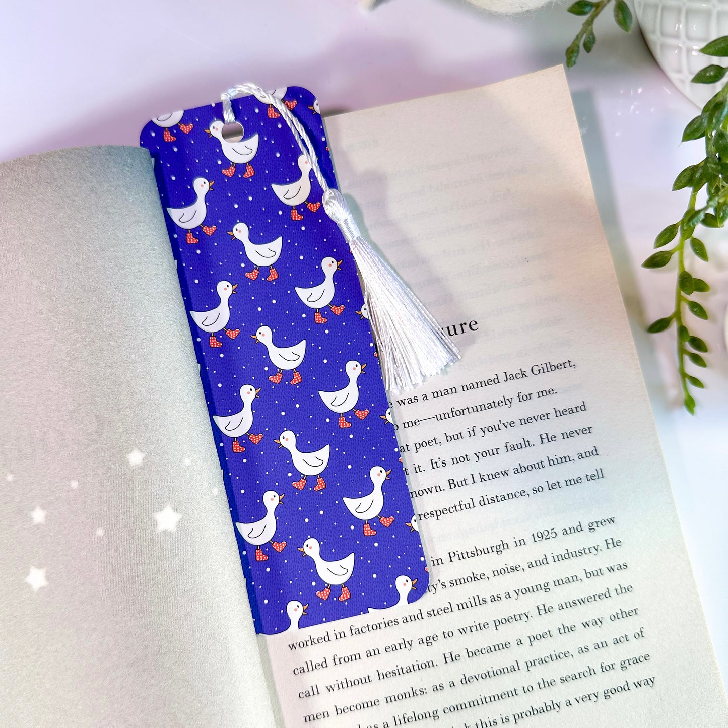 A blue bookmark with a pattern of white ducks, and a white tassel, placed in an open book.