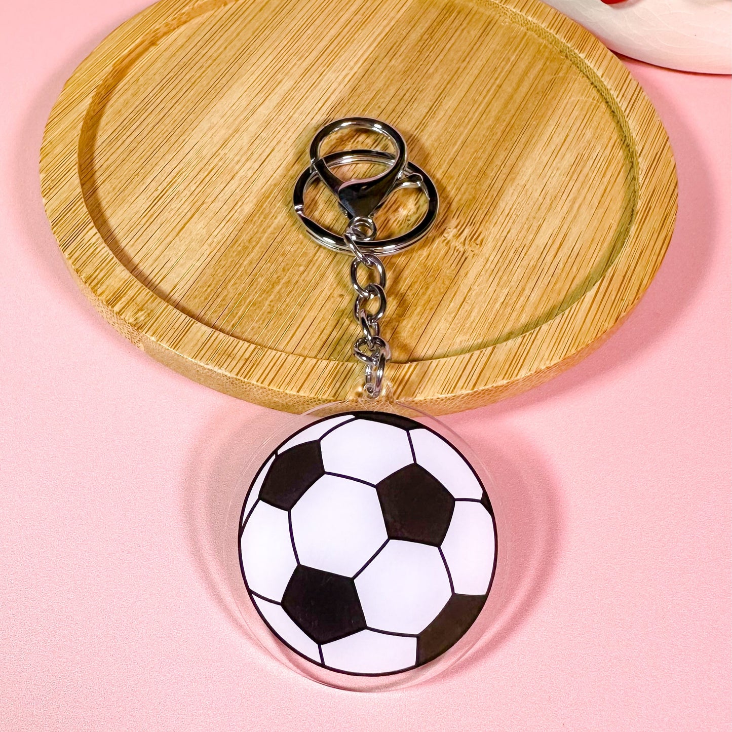 football keychain on a pink background with a wooden coaster