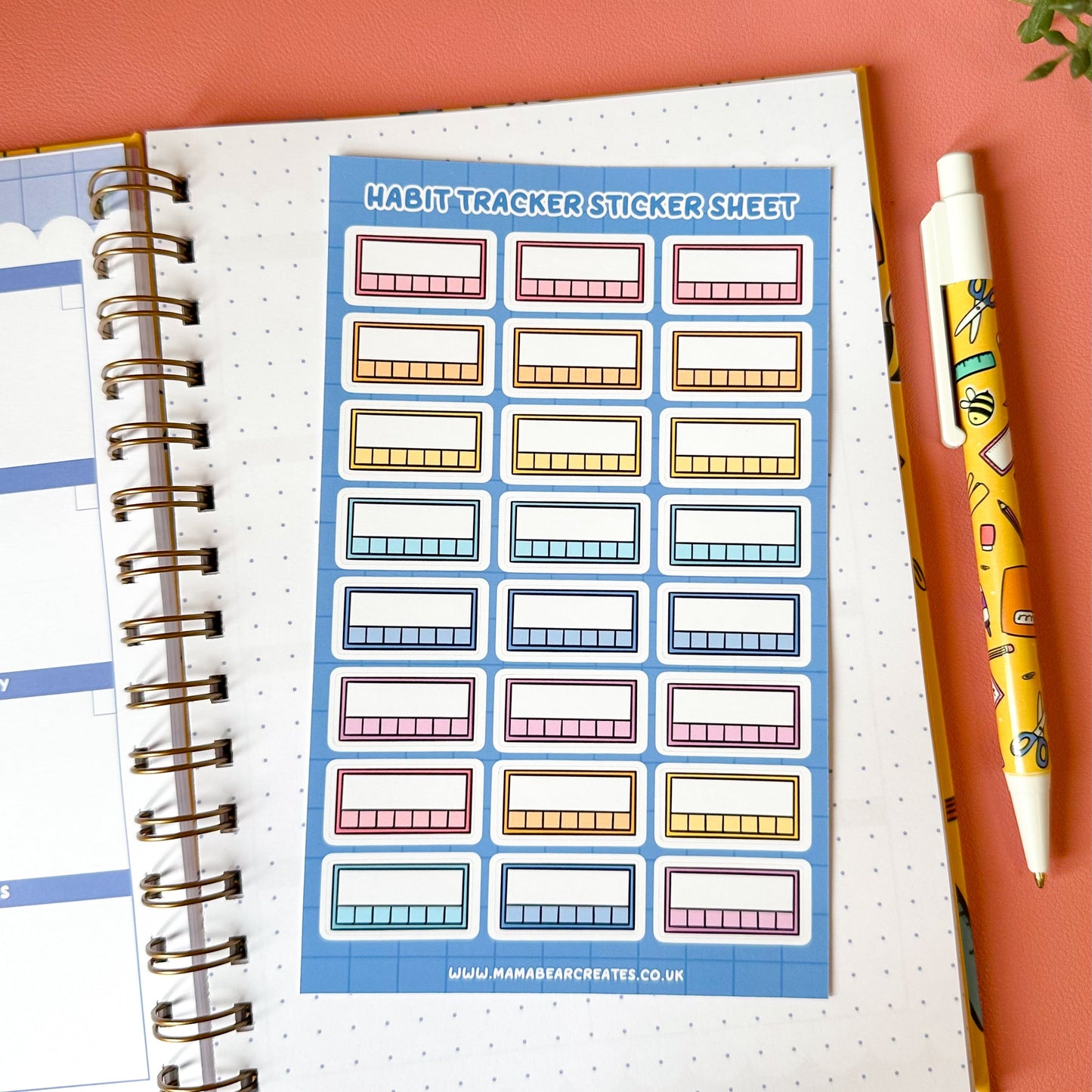 Habit tracker sticker sheet on a planner with a pen and decorative items on a pink background