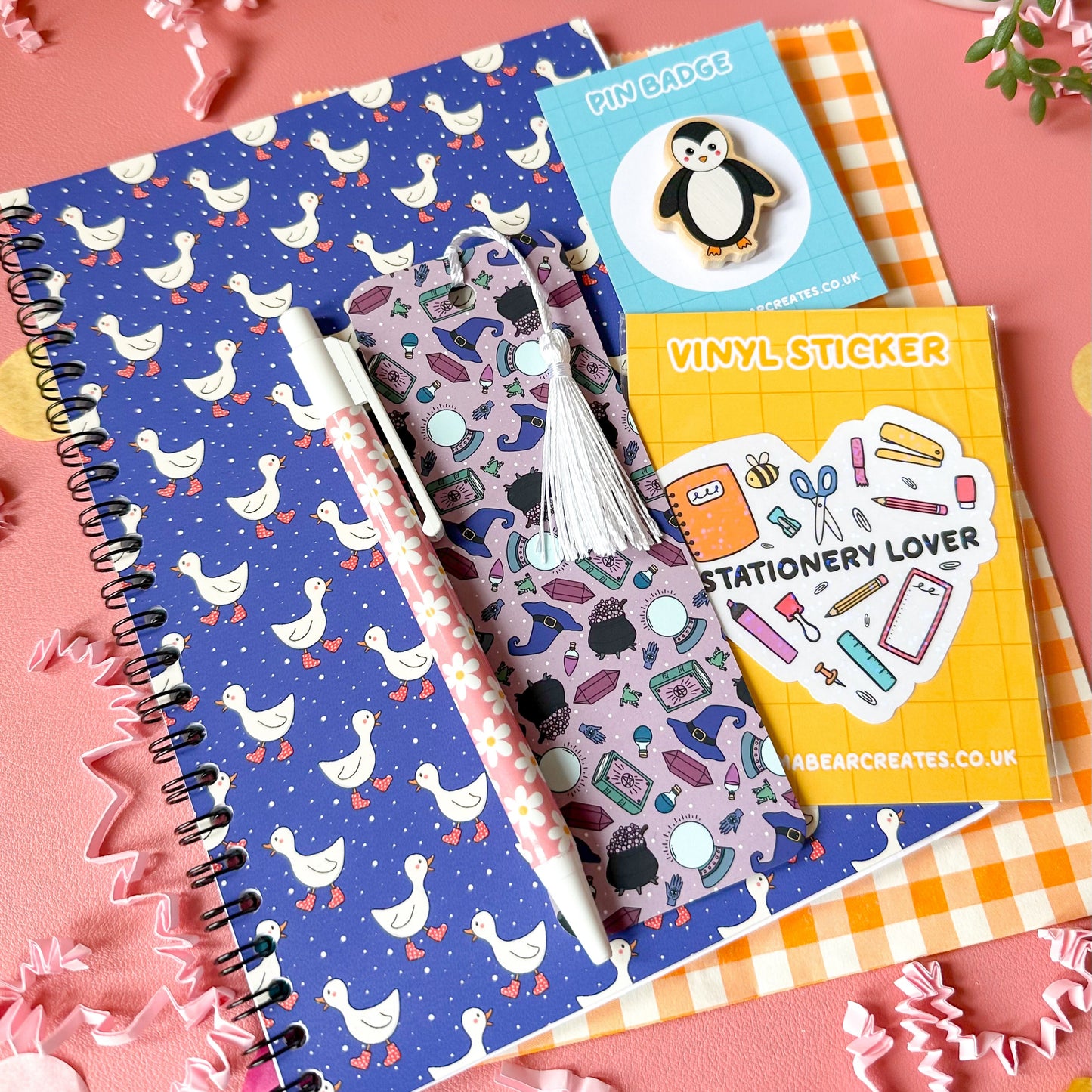 Colorful stationery items including notebooks and a sticker book on a pink background
