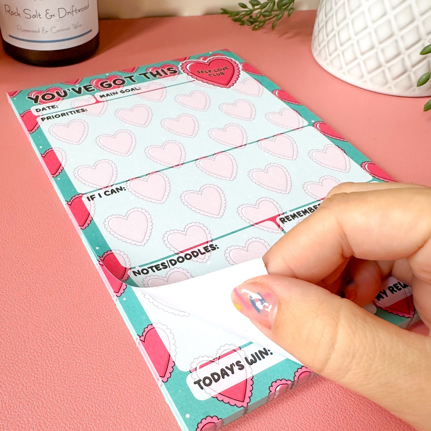 Hand holding a daily planner with heart designs on a pink surface.