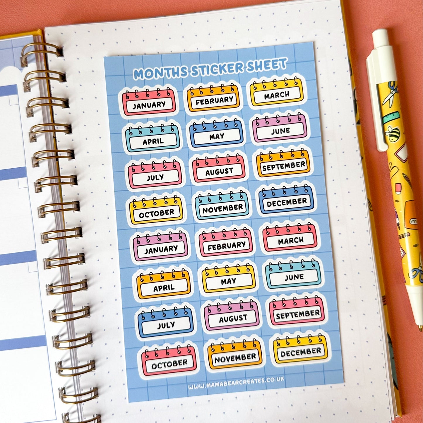 Sheet of colorful monthly stickers on a planner with a pen on a pink background