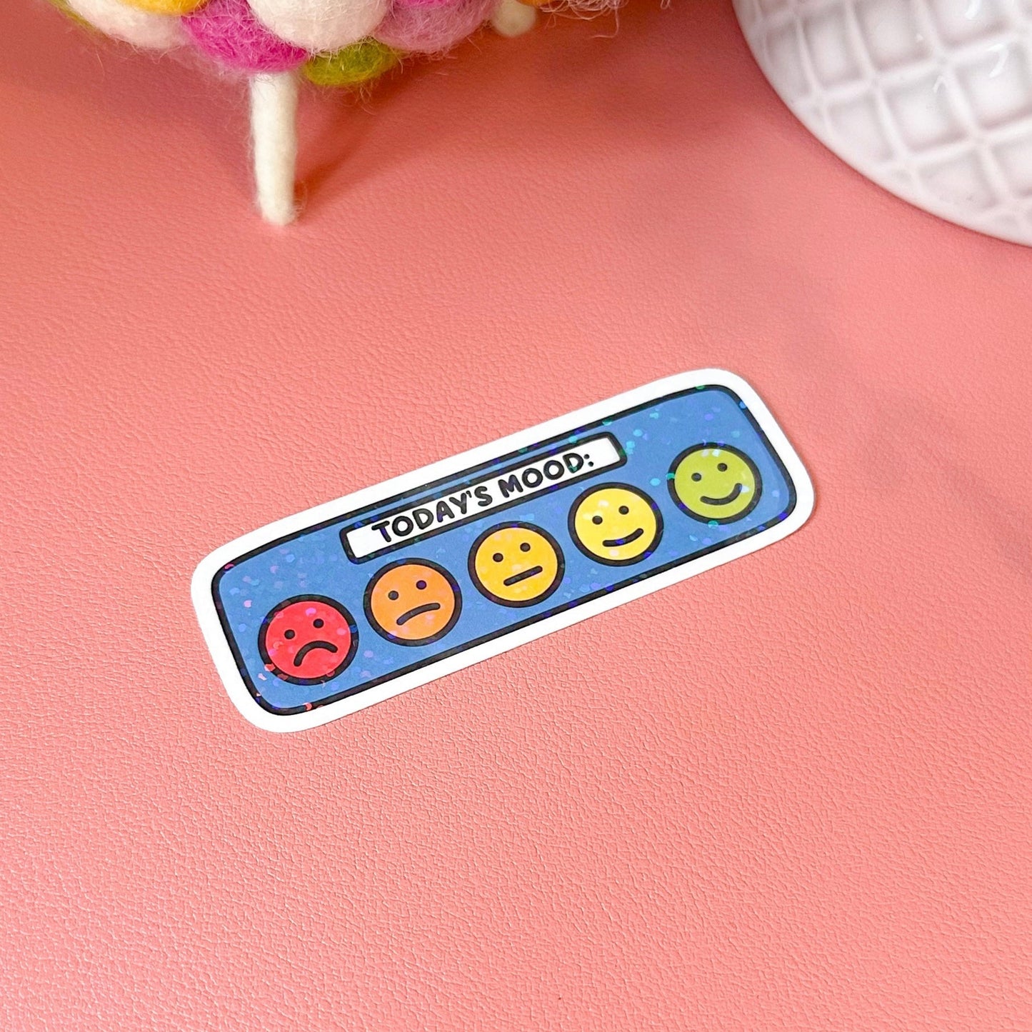 Sticker with smiley face expressions on a pink surface with a plush toy in the background