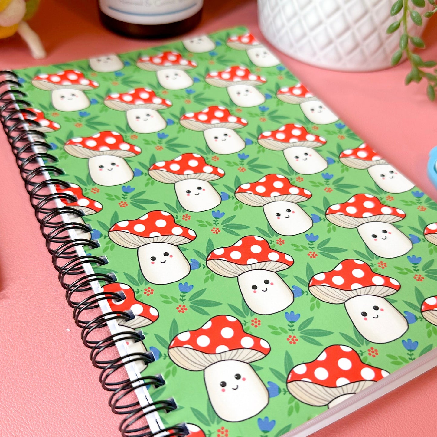 Notebook with a colorful mushroom and ghost pattern on a pink surface.