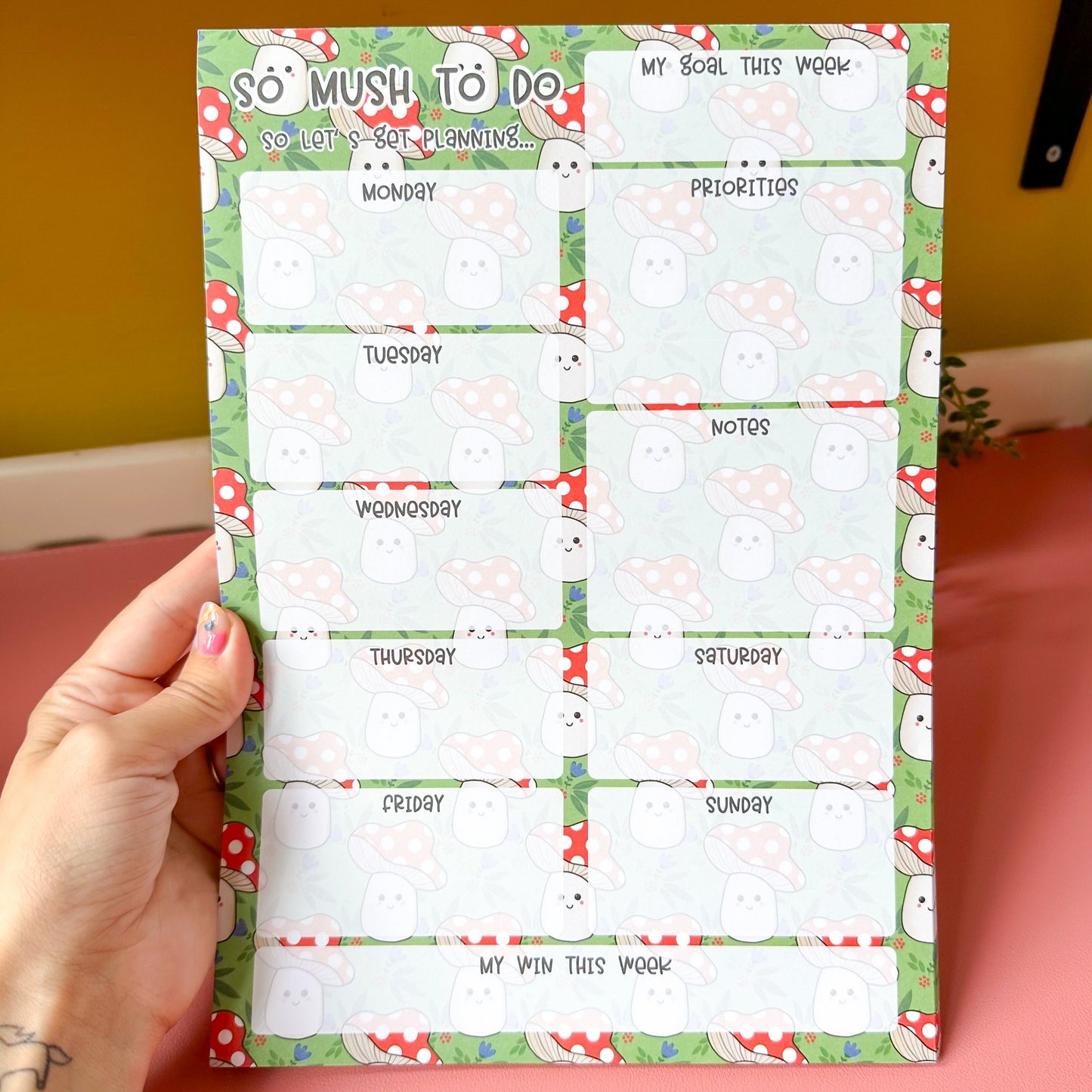 Weekly planner sheet with cartoon mushroom design held by a person.