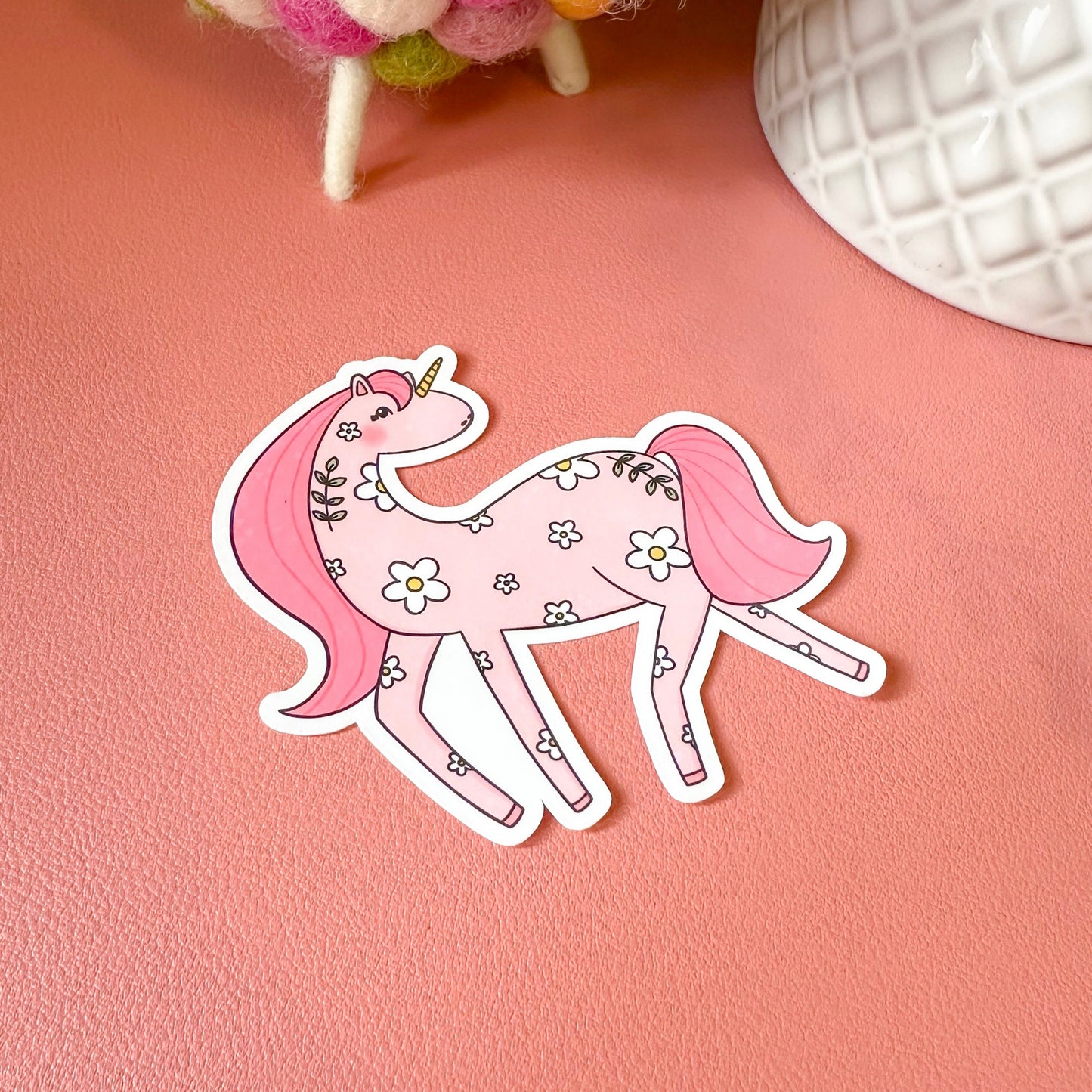 Pink unicorn sticker on a pink surface with decorative items in the background