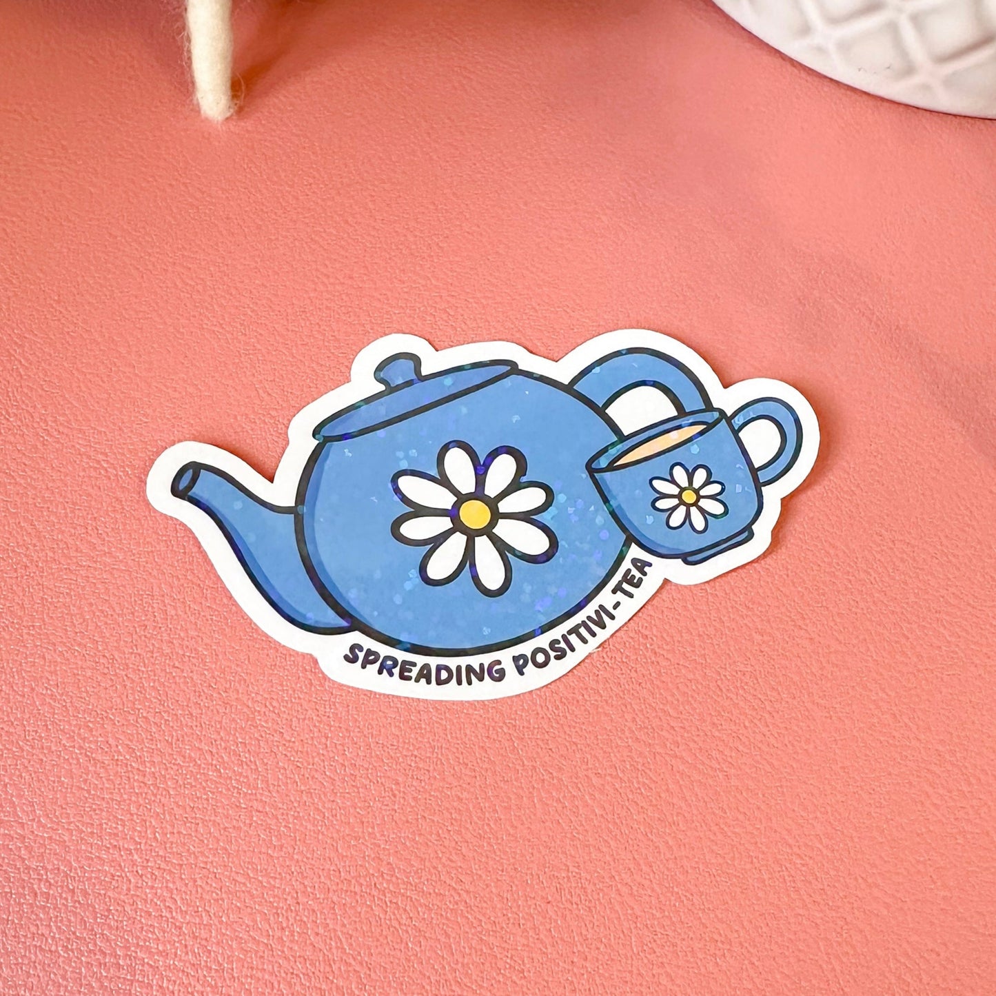 Sticker of a blue teapot with flowers on a pink surface