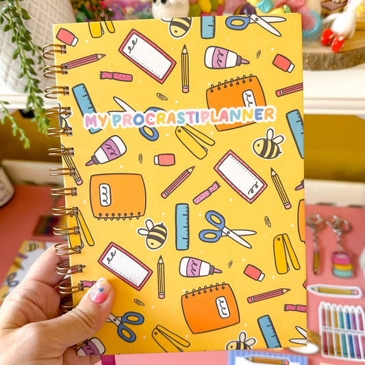 Hand holding a planner with colorful stationery illustrations on a yellow background
