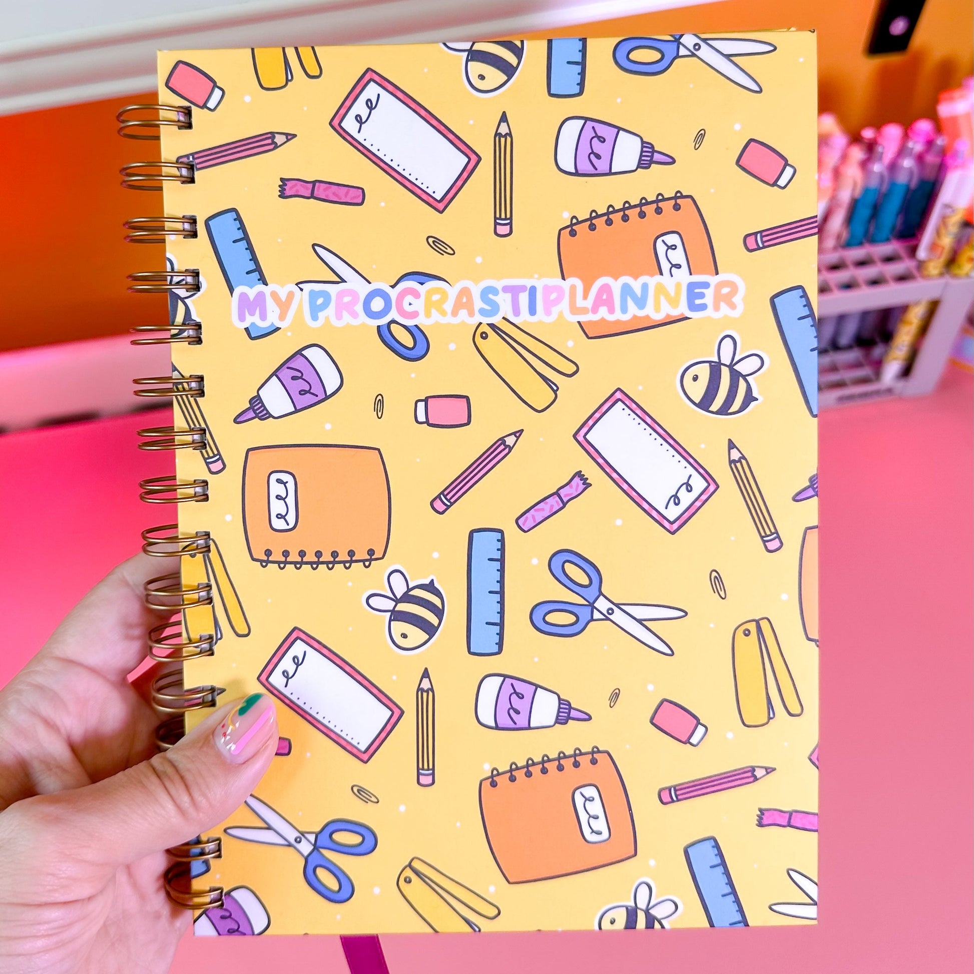 planner with stationery-themed cover held by a hand on a pink background