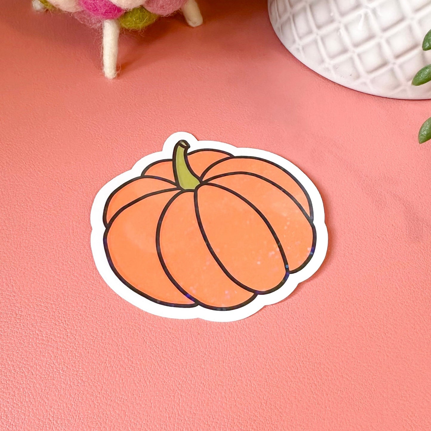 Pumpkin-shaped sticker on a pink surface with decorative items in the background