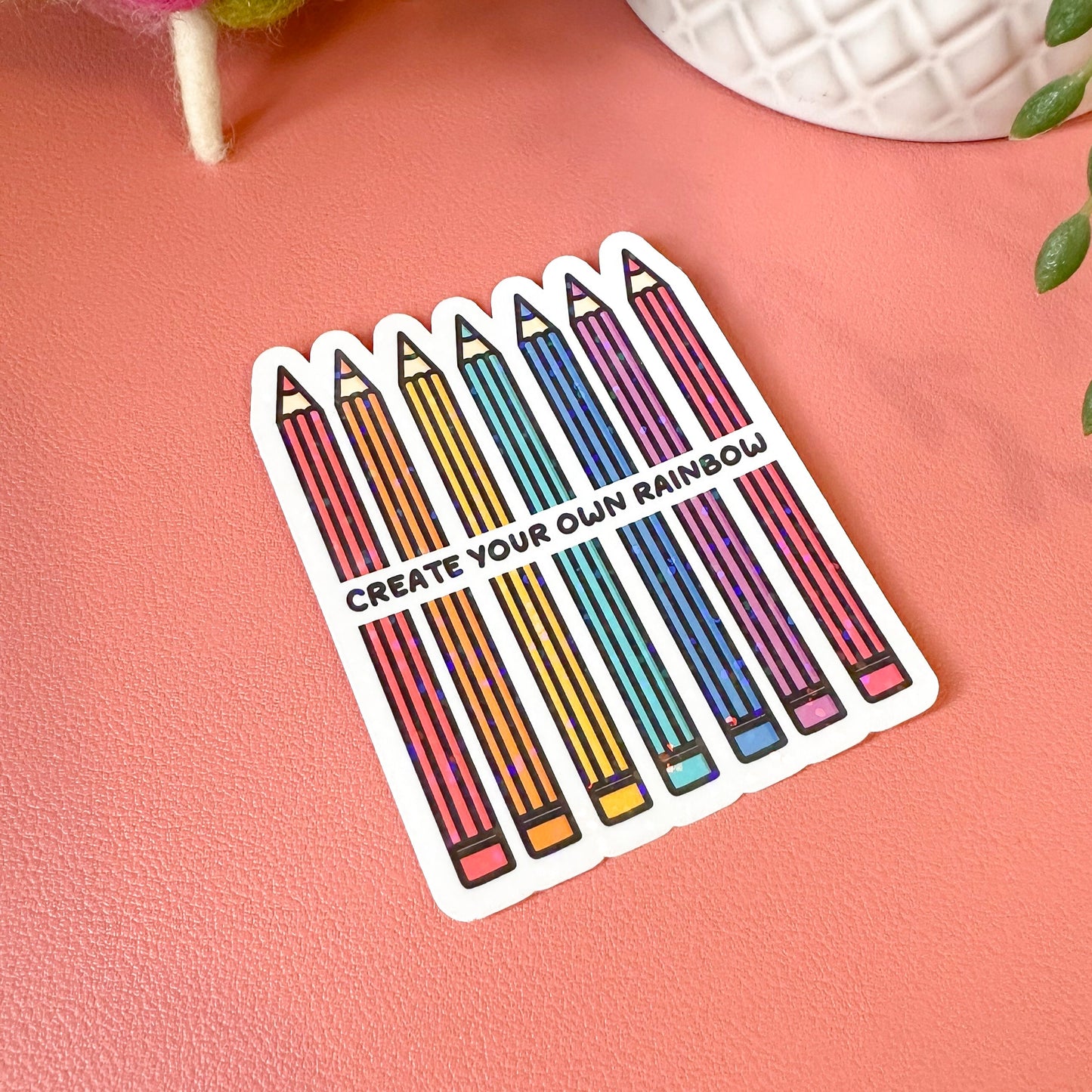 Sticker with colorful pencils and text 'Create Your Own Rainbow' on a pink background