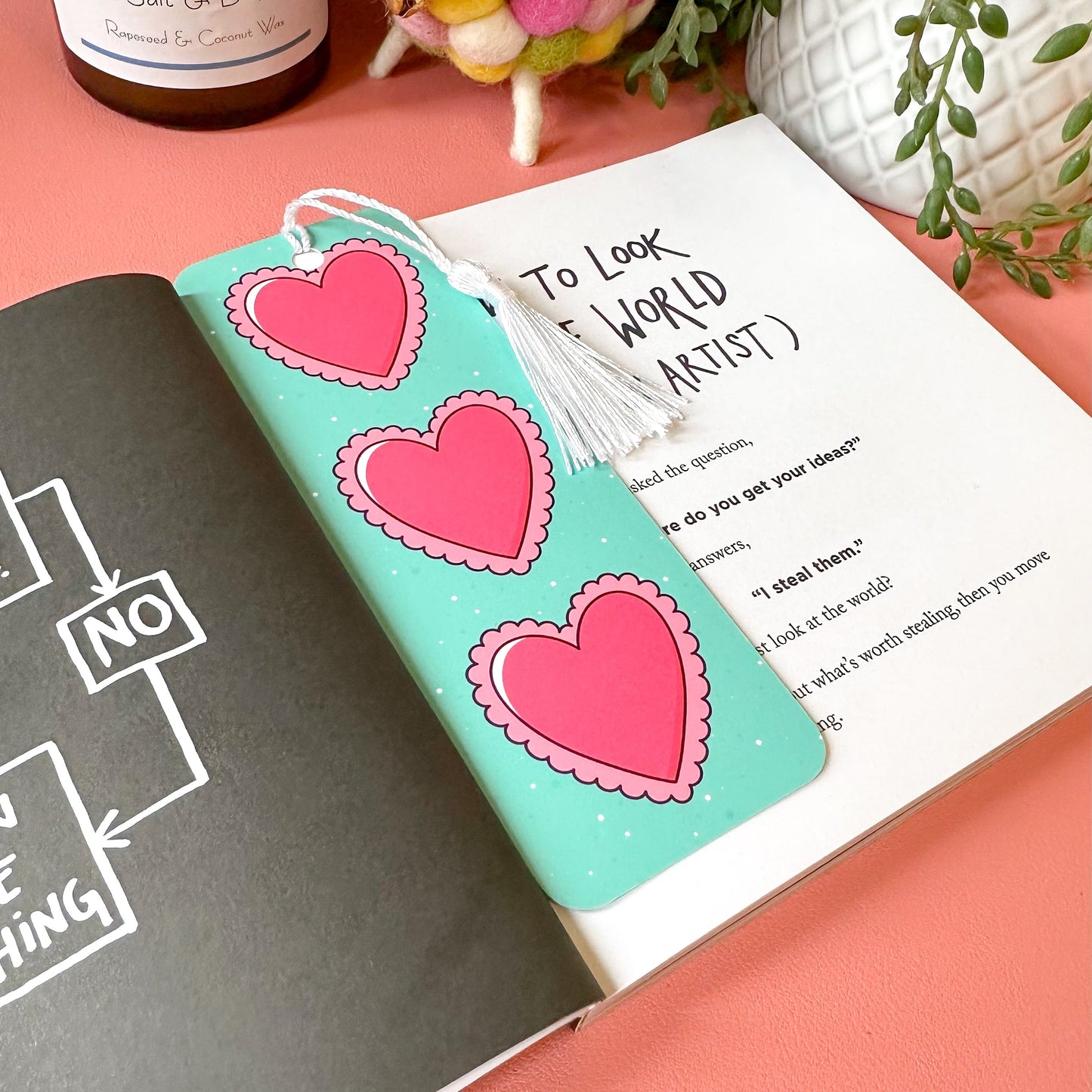 Open book with heart bookmark on a pink surface, next to a bottle of Belles salt and pepper.