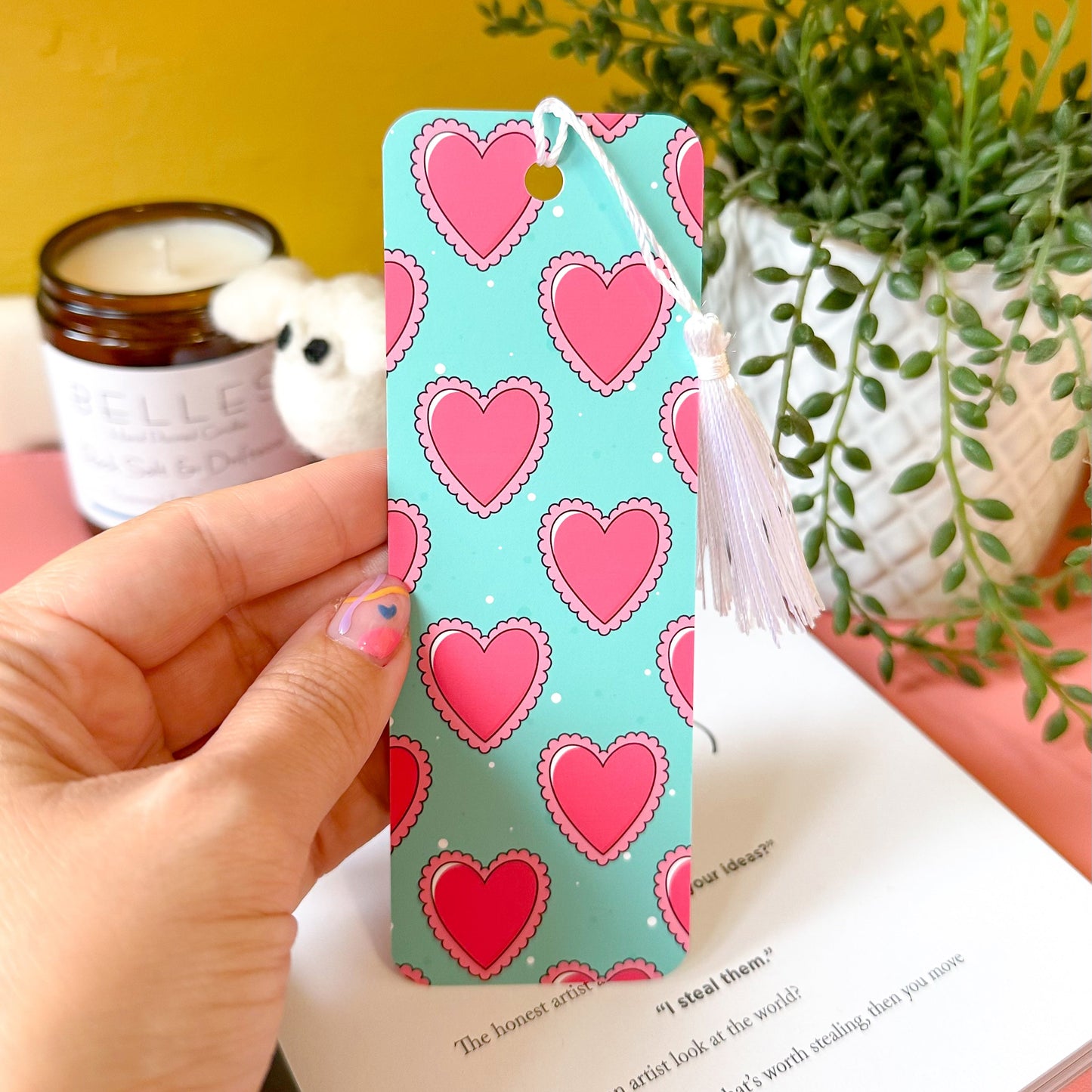 Hand holding a bookmark with heart pattern on a book with a yellow background