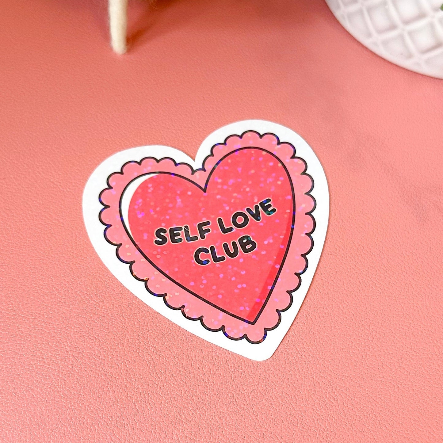 Heart-shaped sticker with 'Self Love Club' text on a pink background
