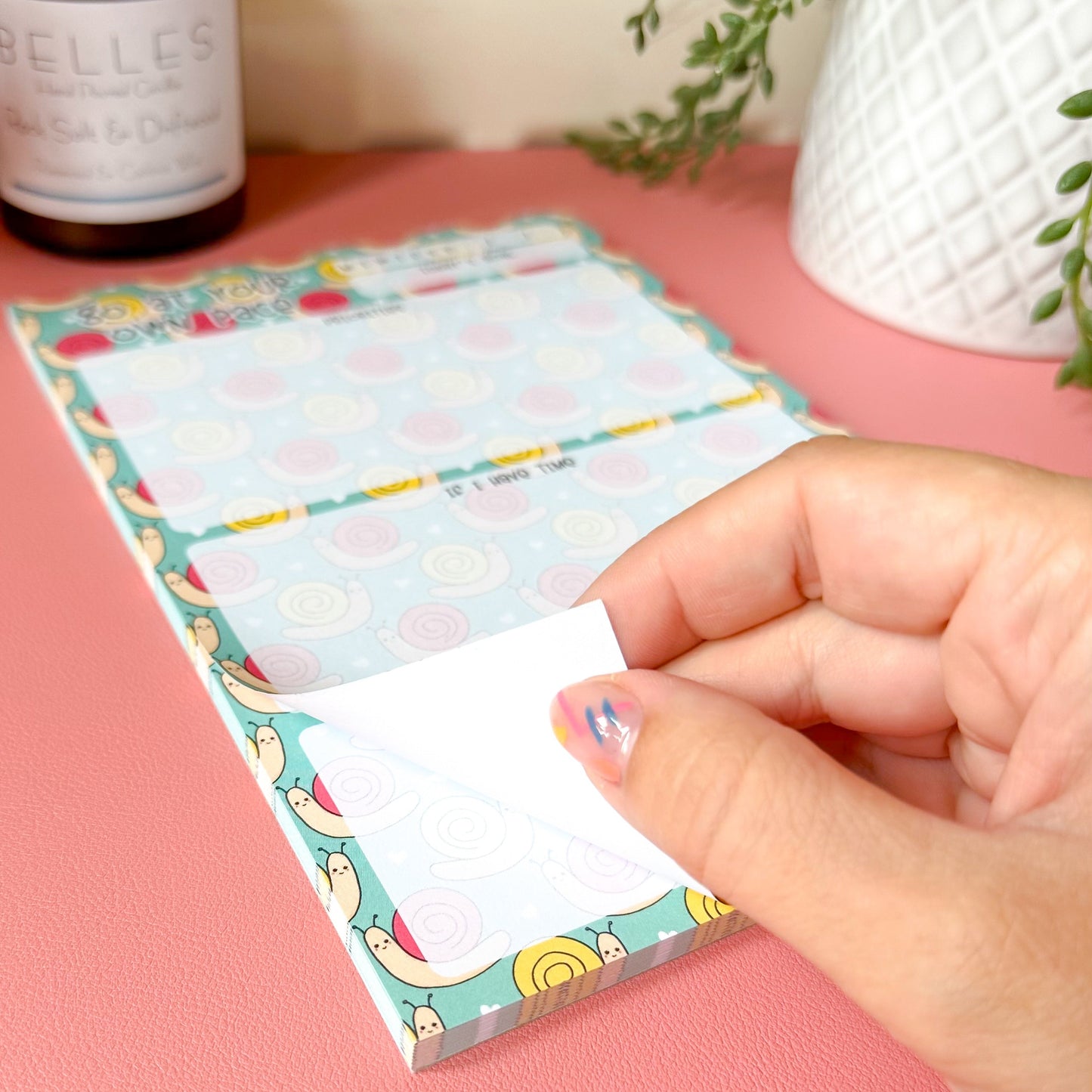 Hand holding a colorful notepad with a pink background