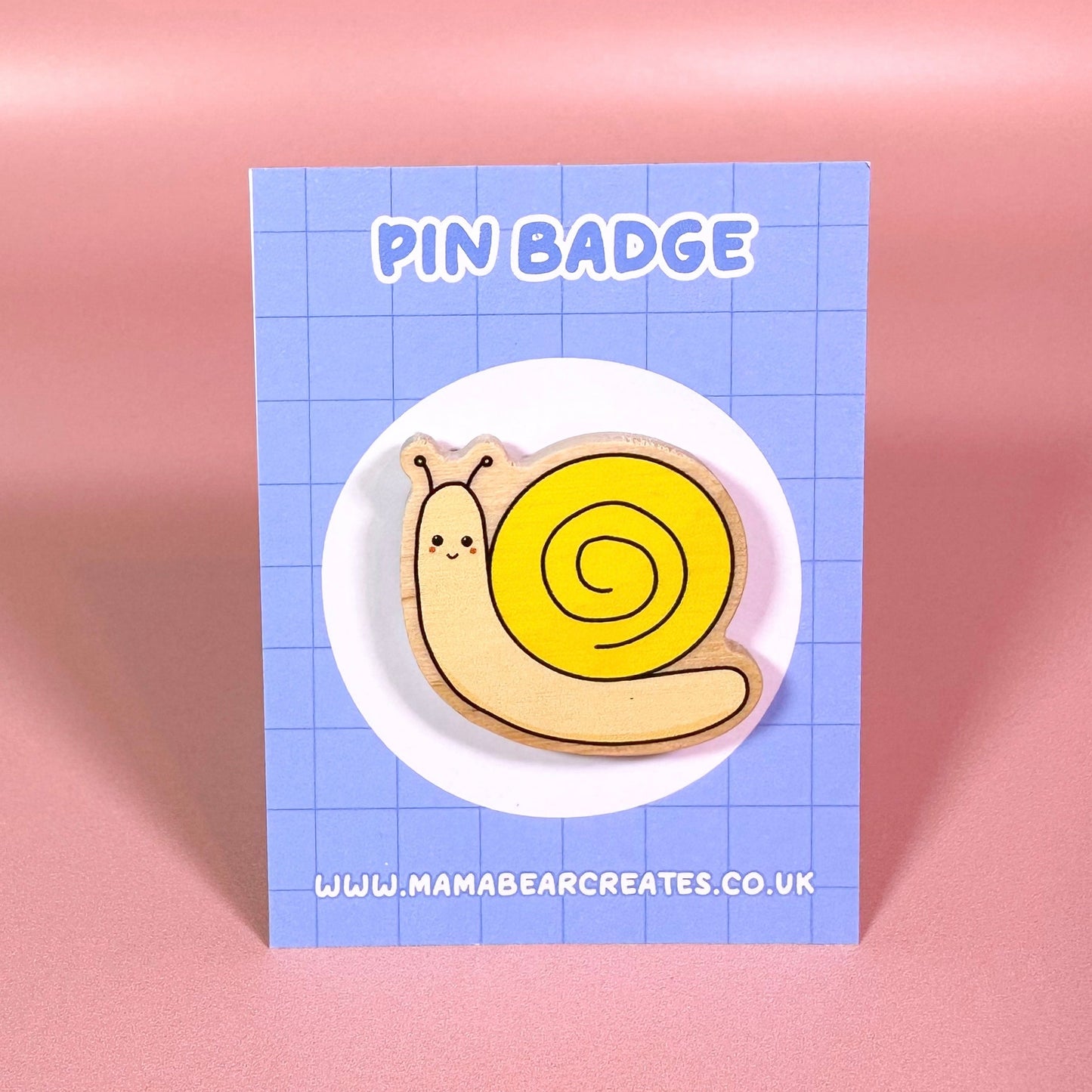 Pin badge of a cartoon snail on a blue card with 'Mama Bear Creates' branding.