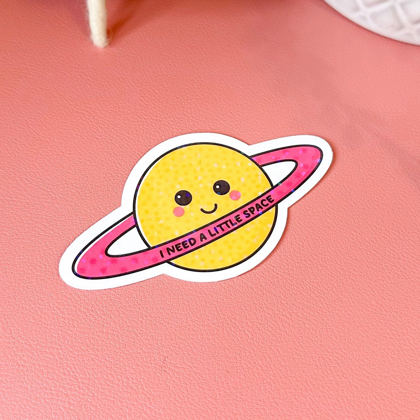 Sticker of a smiling planet with a pink ring on a pink background