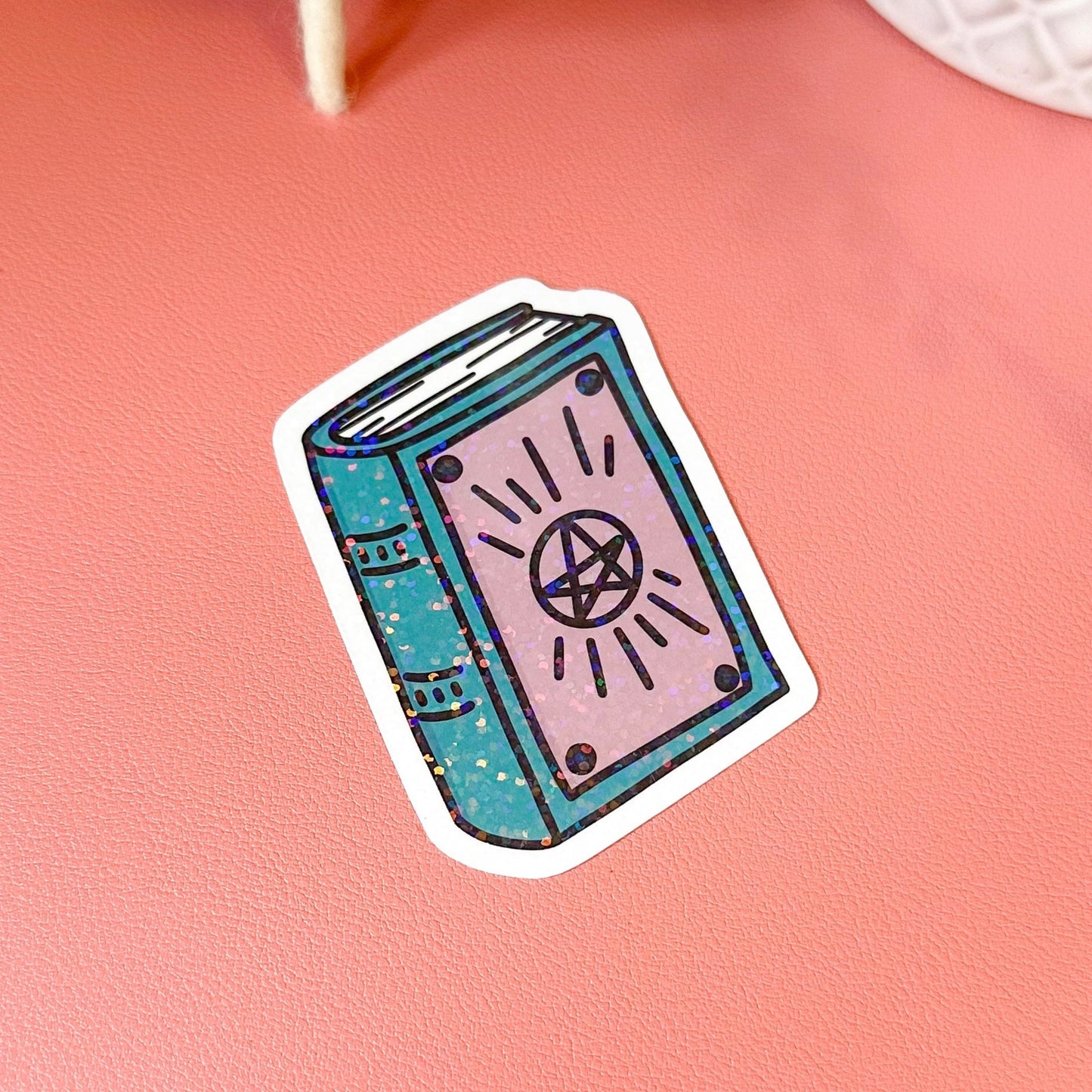 Sticker of a blue book with a pentacle symbol on a pink surface