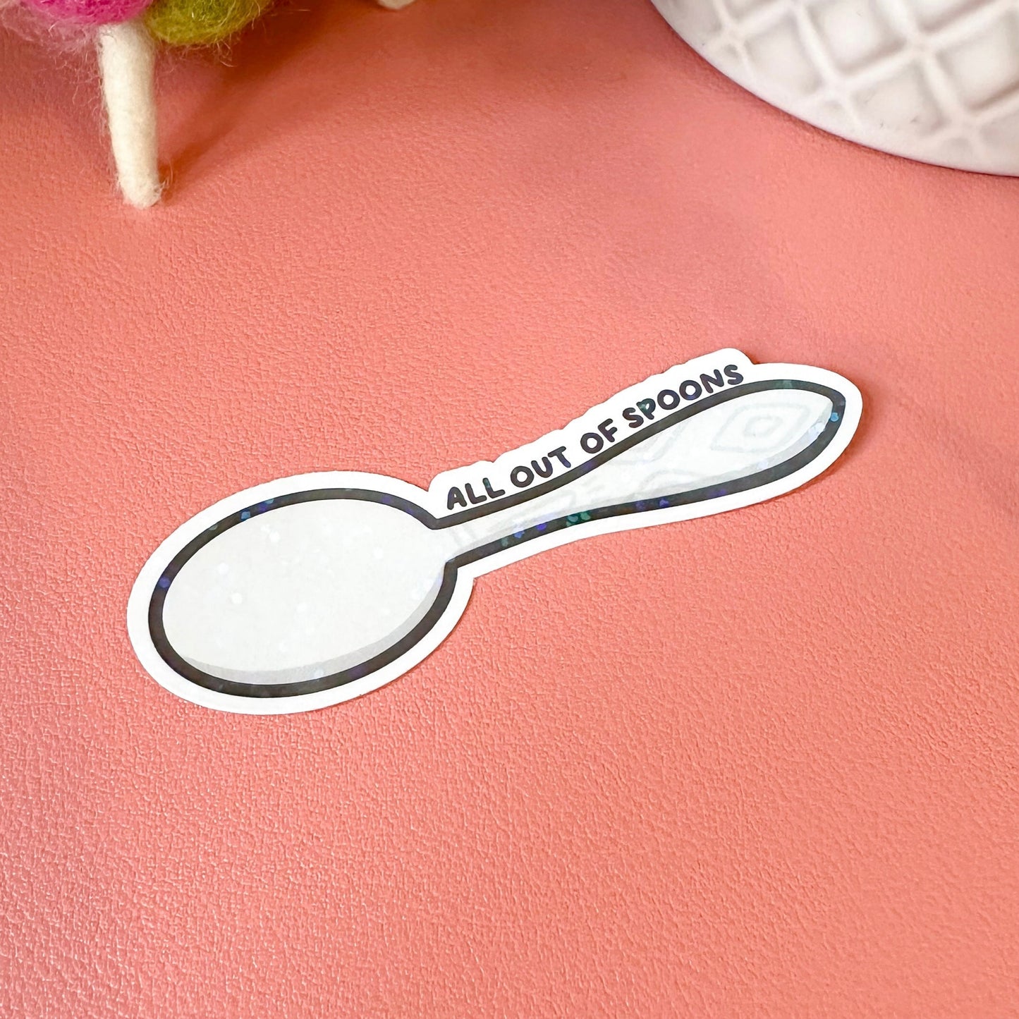 Sticker shaped like a spoon with 'All Out of Spoons' text on a pink surface.