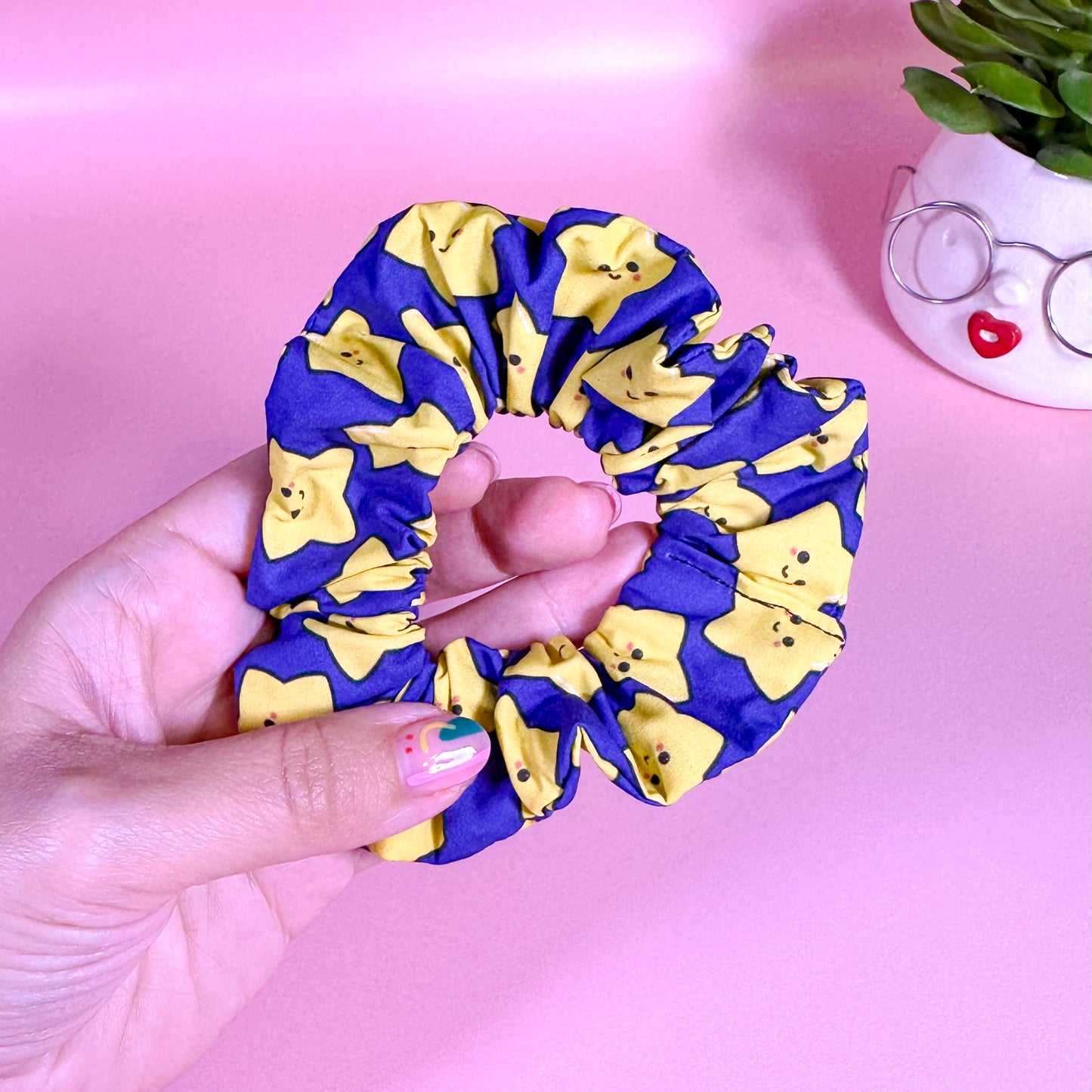 Hand holding a blue and yellow scrunchie against a pink background