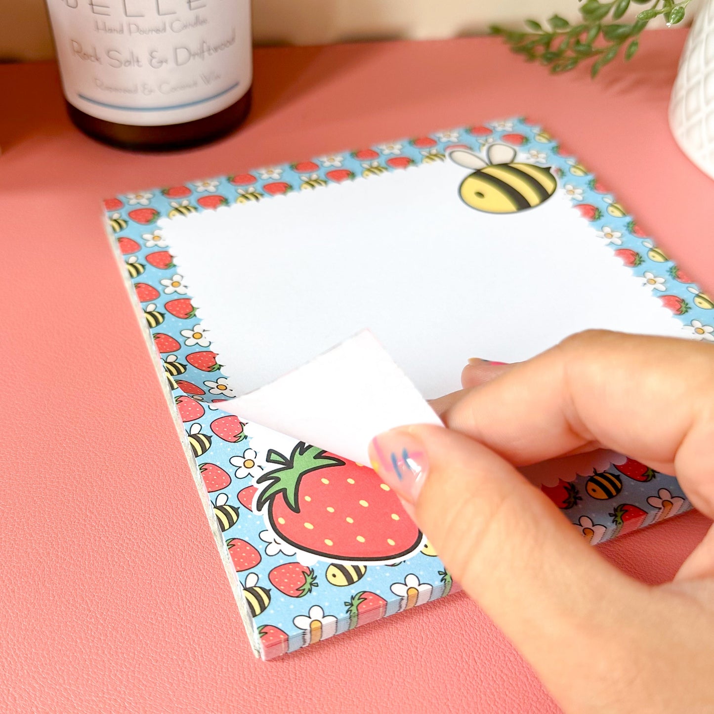 Hand holding a strawberry-themed notepad with a pink background