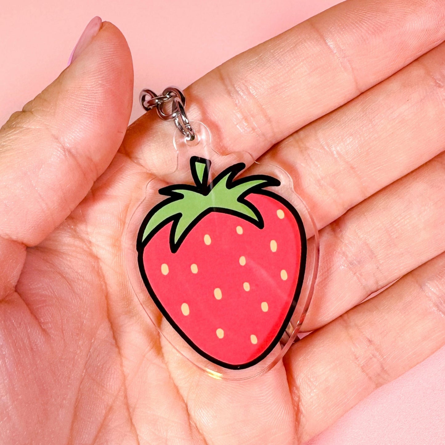 Strawberry-shaped keychain held in a hand against a pink background