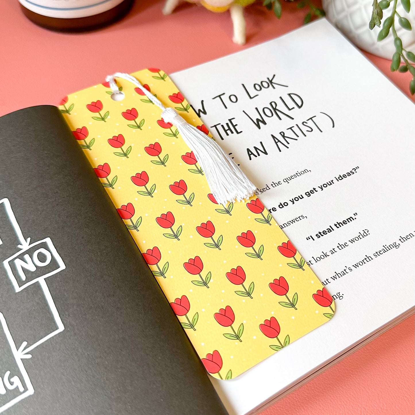 tulip bookmark on a pink surface with a candle and plant in the background.