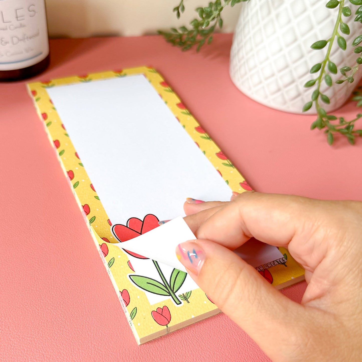 Hand holding a decorative notepad with tulip and flower designs on a pink surface.