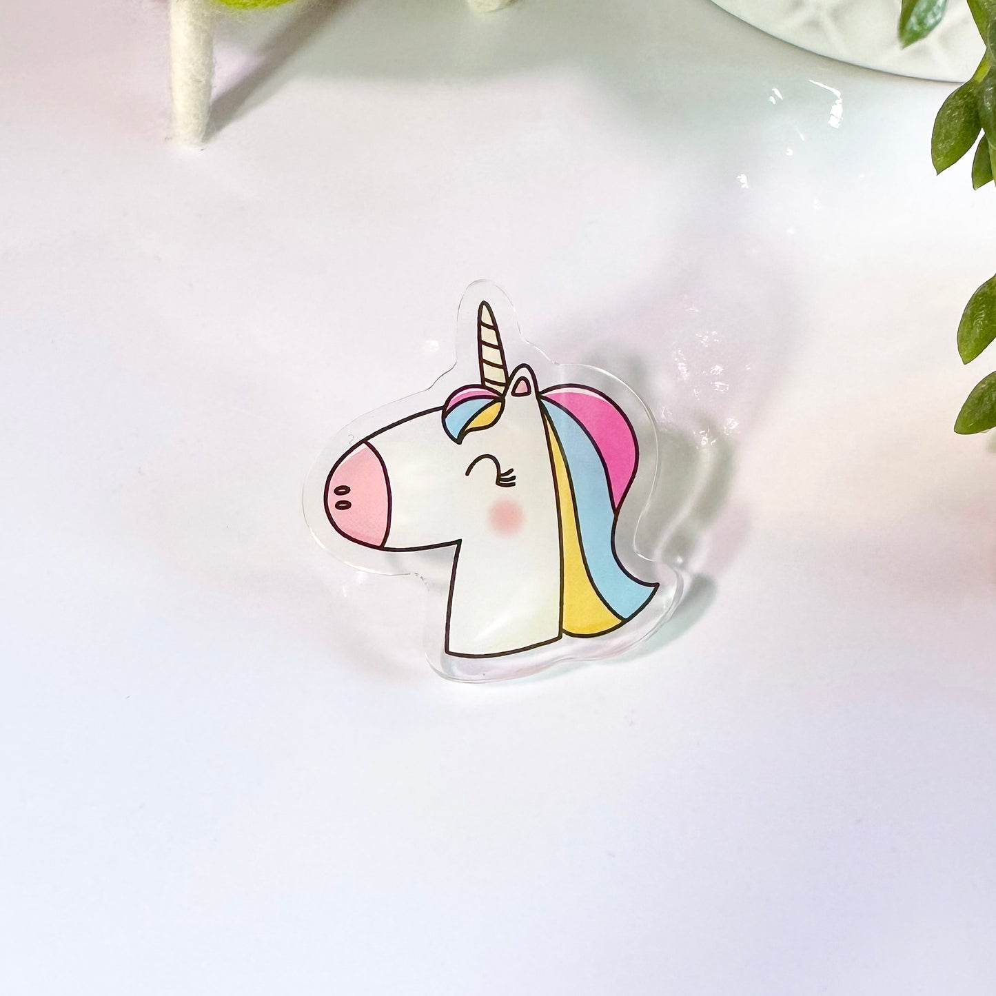 A colorful acrylic pin badge depicting a smiling unicorn on a desk