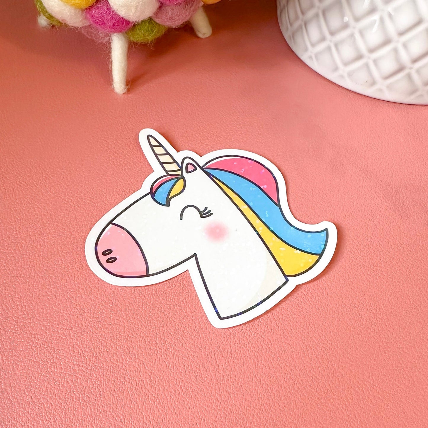 Cartoon unicorn sticker on a pink surface with colorful plush toys in the background