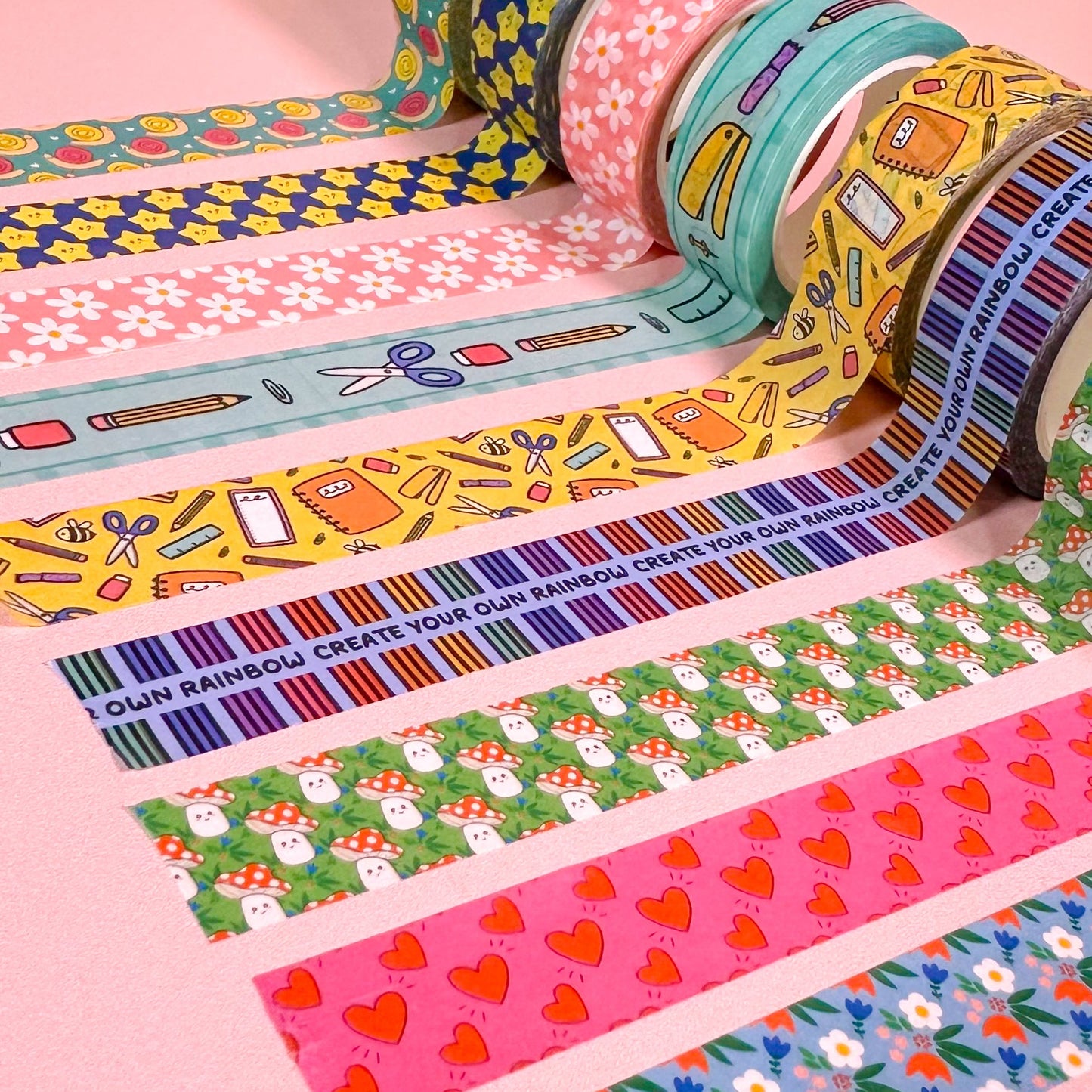 Colorful washi tape rolls with various patterns on a pink background