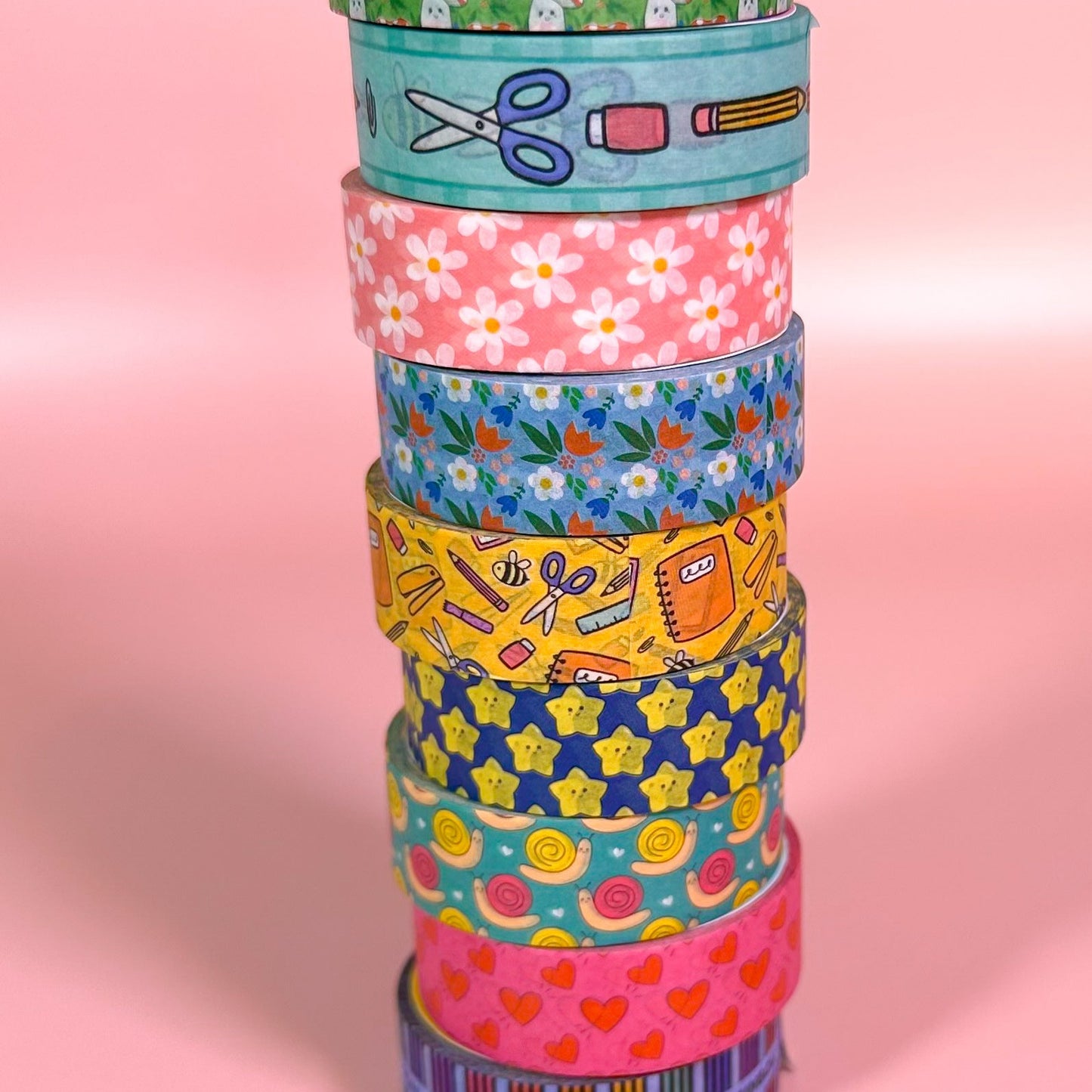 Stack of colorful washi tape rolls on a pink background