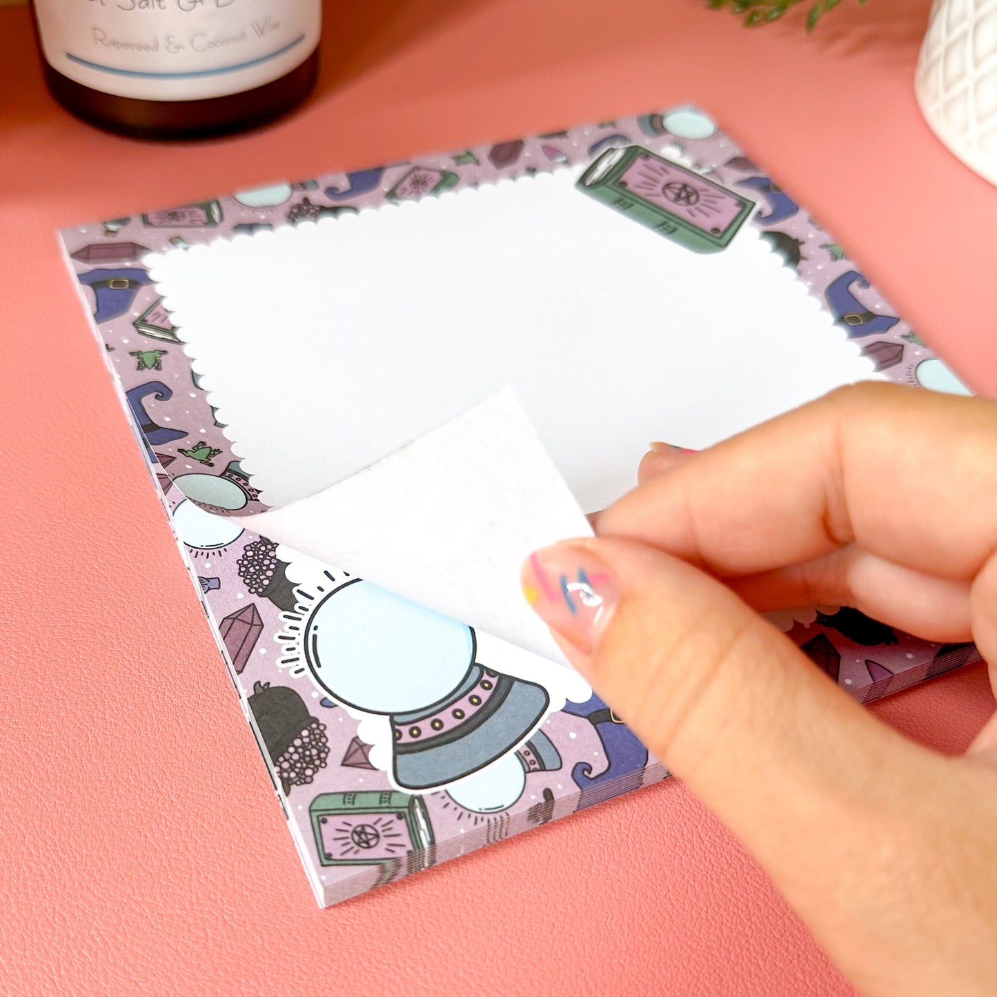 Hand holding a witchy notepad on a pink surface.