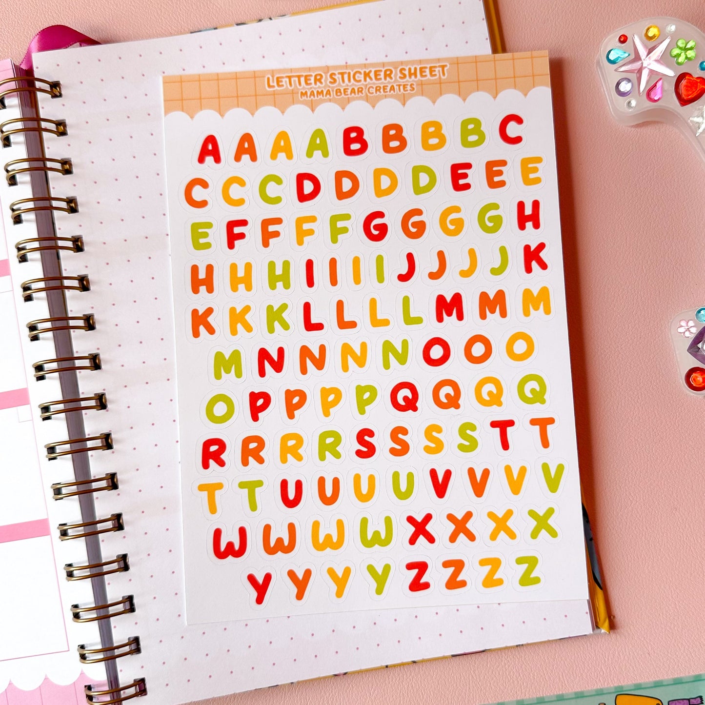 Colorful letter stickers on a notebook with stationery items on a pink background