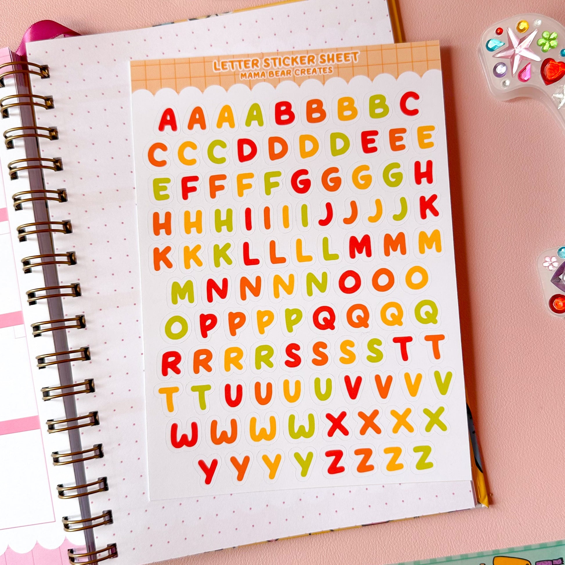Colorful letter stickers on a notebook with stationery items on a pink background
