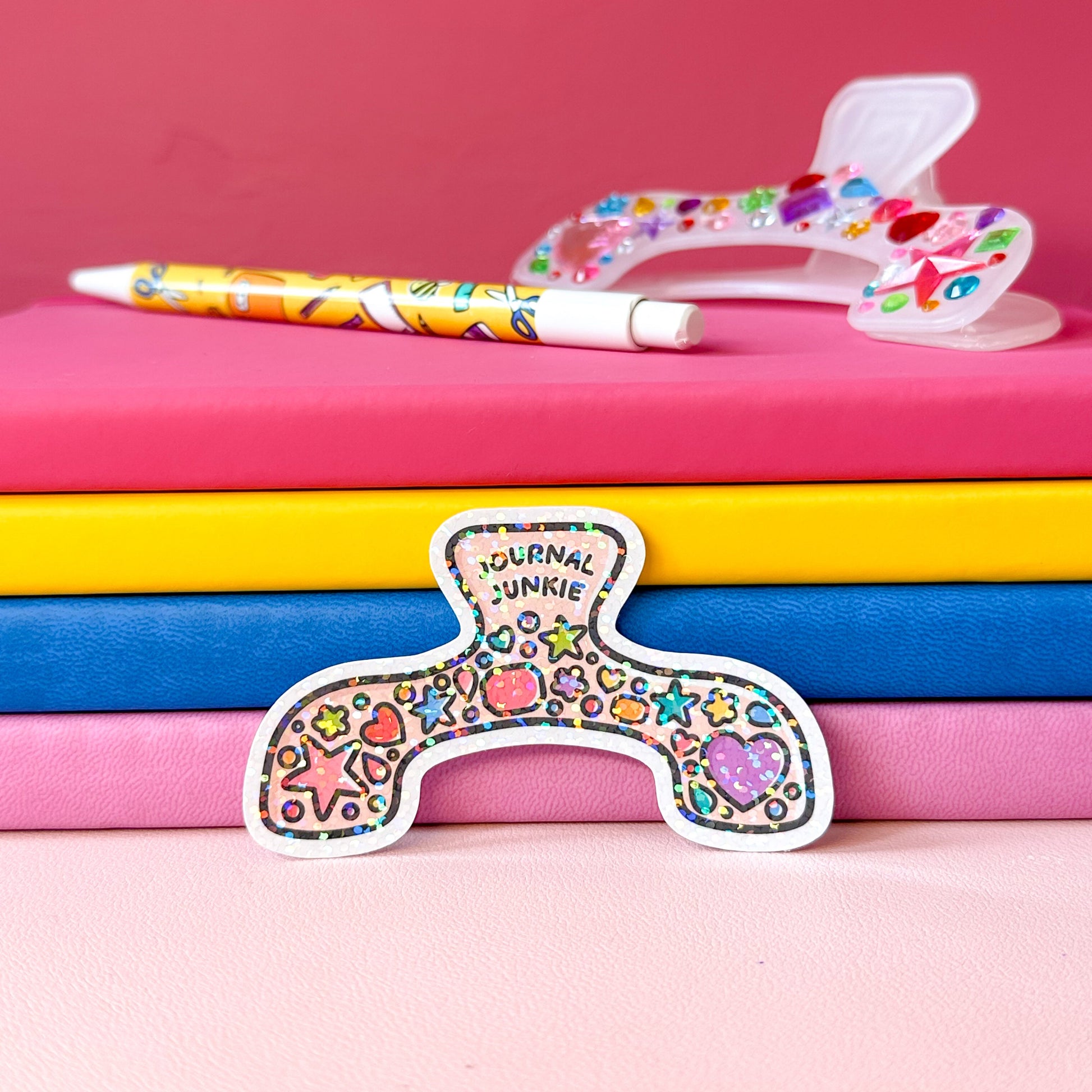 Colorful stationery items including a pen, colorful heart-patterned object, and 'Journal Junkie' sticker on pink and blue notebooks.